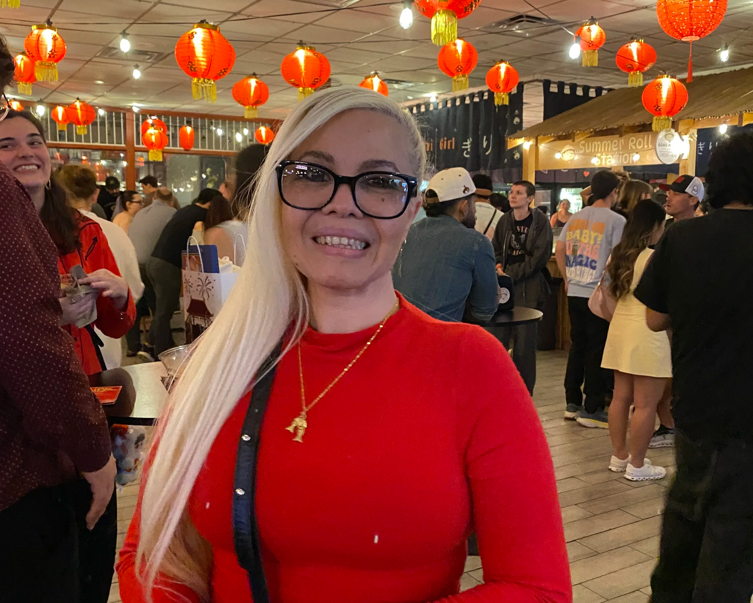 People gathered at a lively indoor festival decorated with red lanterns hanging from the ceiling, with some people smiling and interacting.