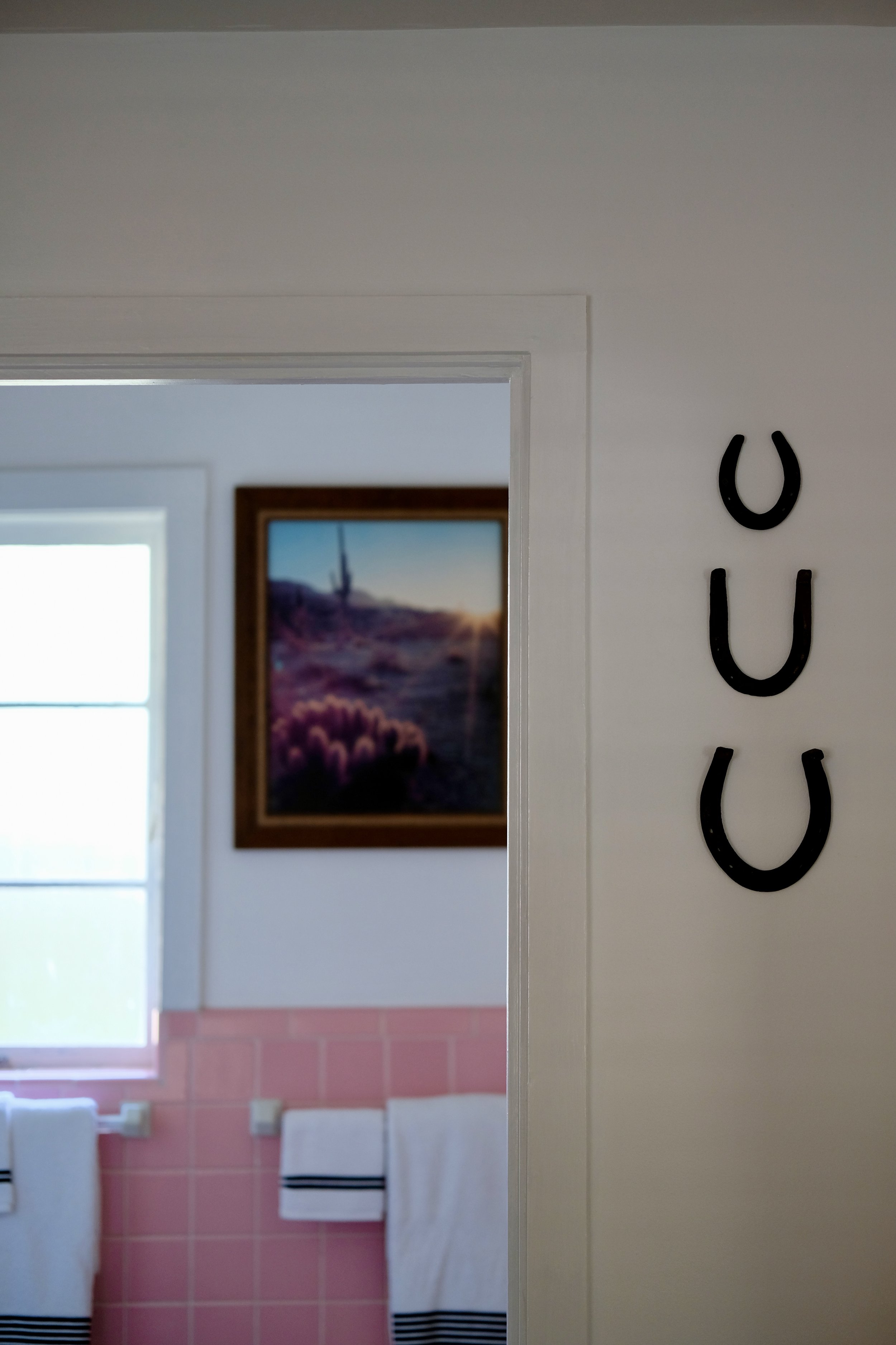 View into the pink-tiled bathroom of Room 11, with artwork and black horseshoe details installed for Room for Strangers™.