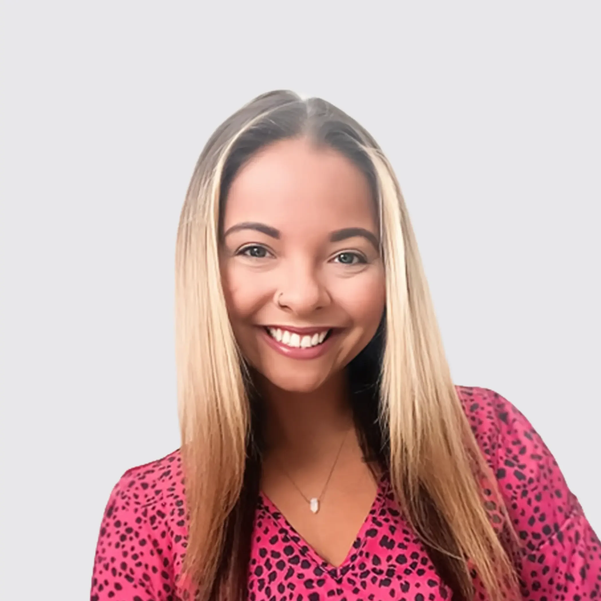 Young woman with long blonde hair smiling, wearing a pink and black spotted top, with a neutral background.