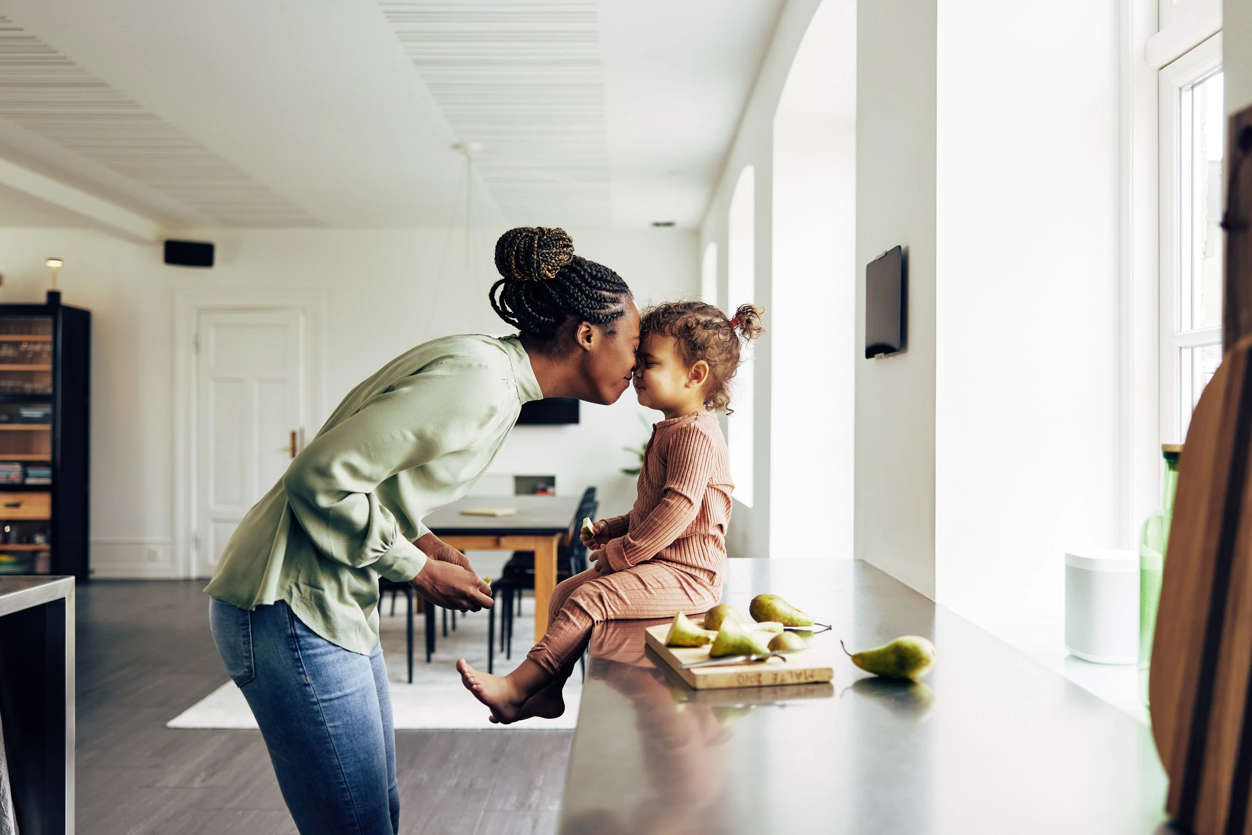A mom leaning forward and touching foreheads with a young girl sitting on a kitchen counter, working on communication skills learned during in-home speech therapy for kids in Vista, CA.