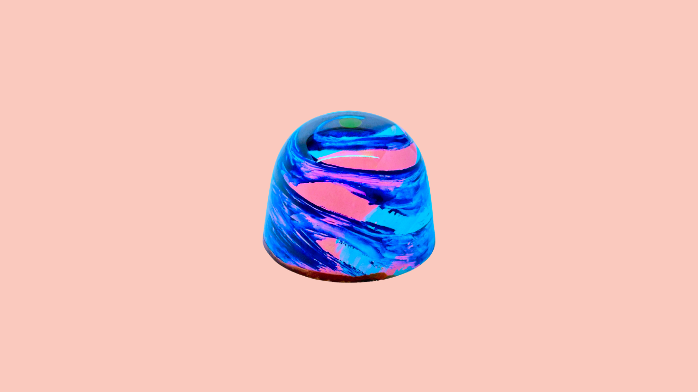 Colorful glass paperweight with swirling blue and pink patterns on a peach background.
