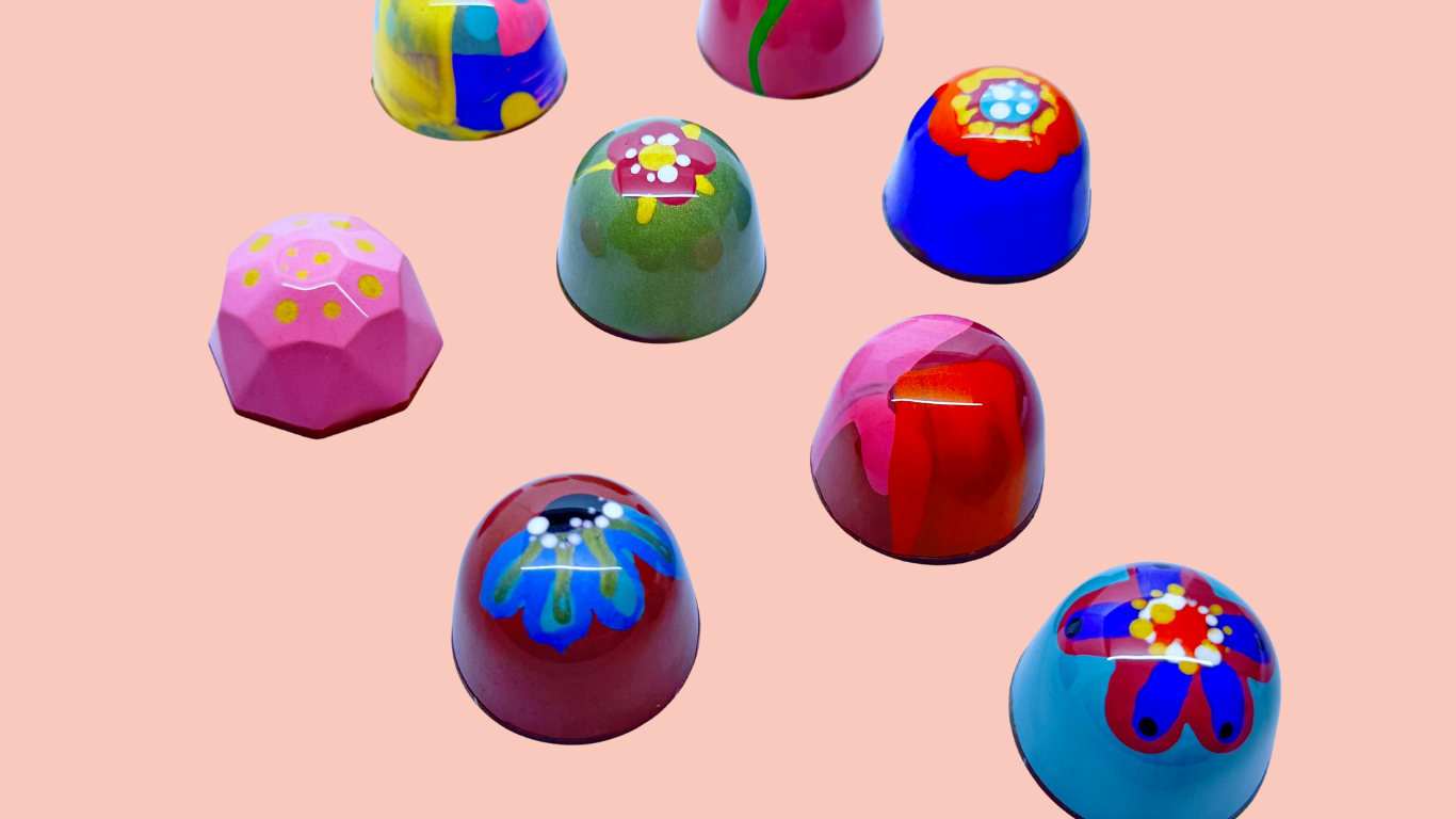 Colorful, decorated chocolate bonbons on a pink background.