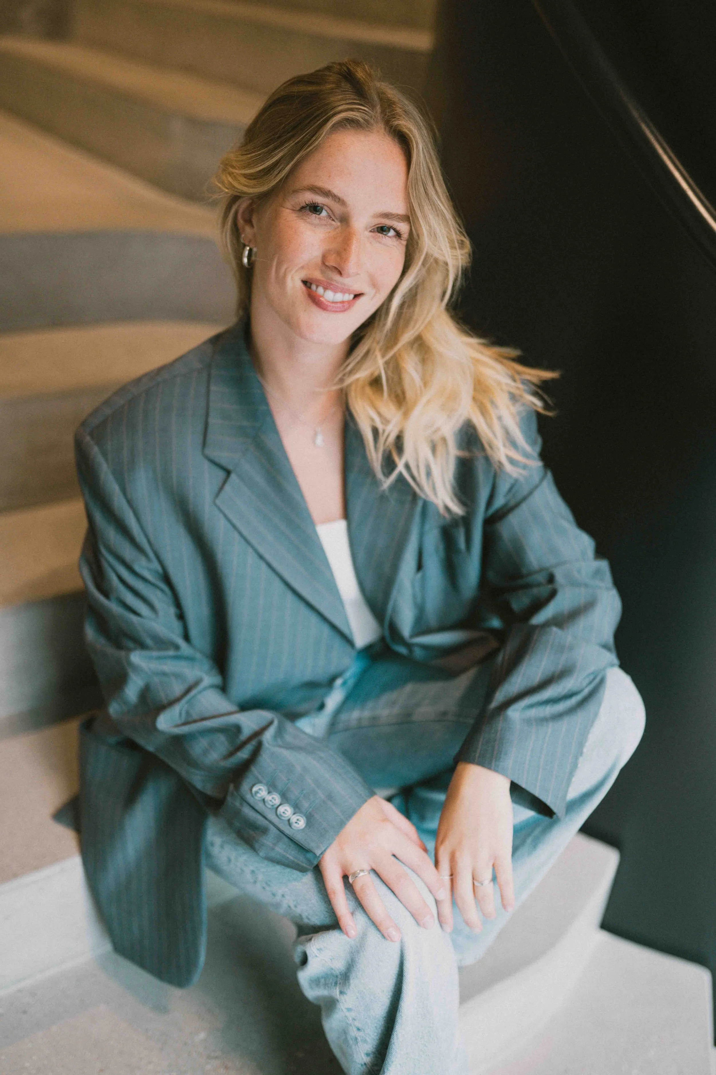 Caro Nowak sitzend, lächelnd im grauen Blazer
