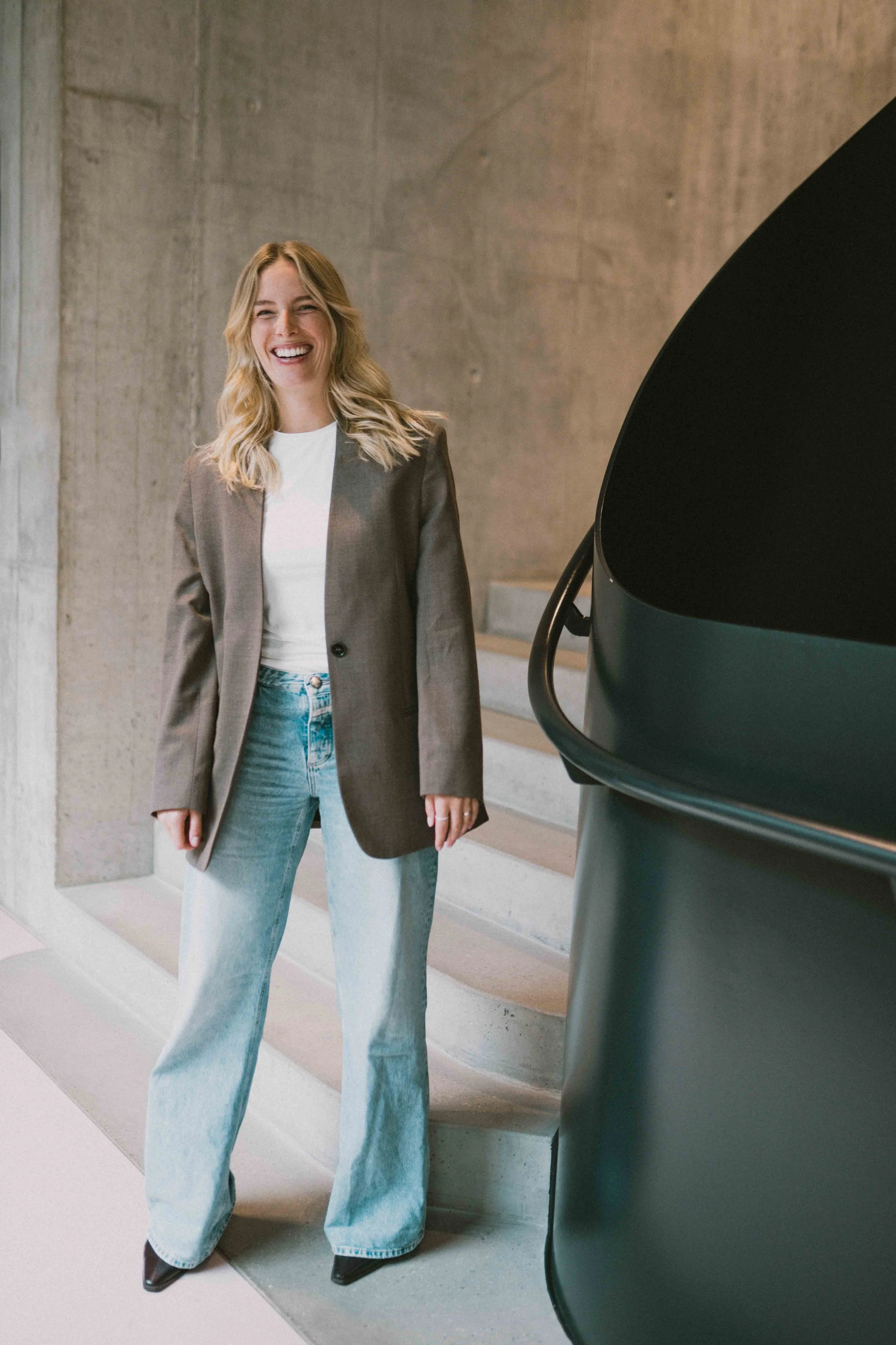 Caro Nowak im braunen Blazer und Jeans, gehend auf einer Treppe