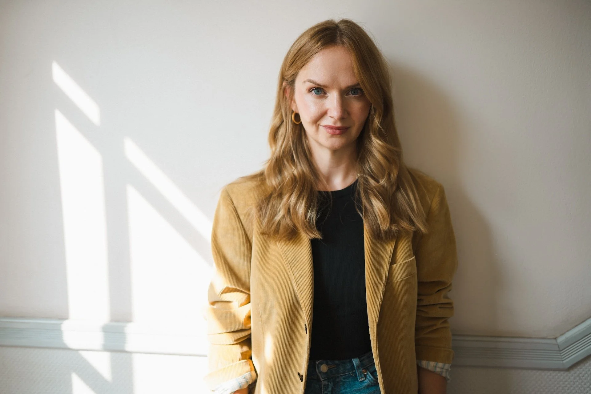 Porträt von Kristina Lunz in senffarbenem Cord-Blazer vor heller Wand