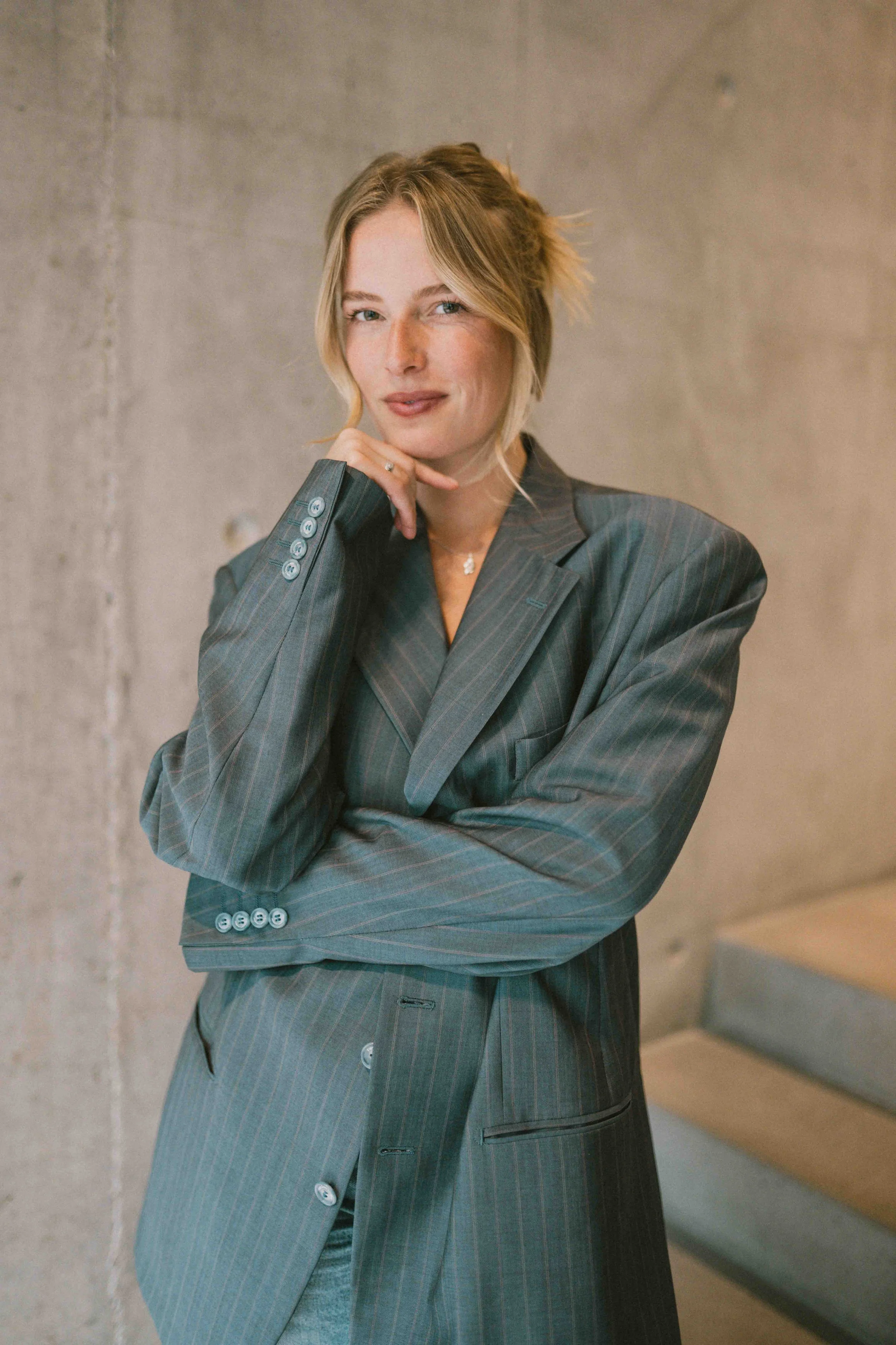 Porträt von Caro Nowak im grauen Nadelstreifen-Blazer vor Betonwand