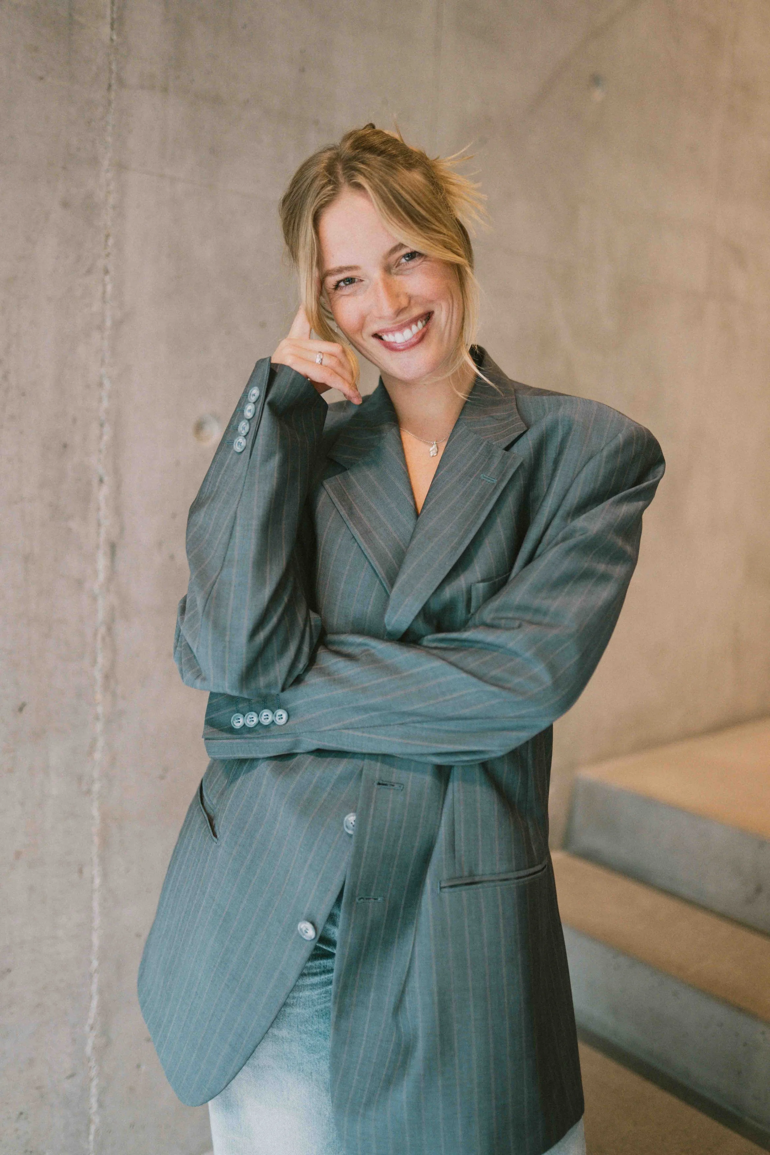 Caro Nowak lachend mit Hand am Kopf, im grauen Blazer