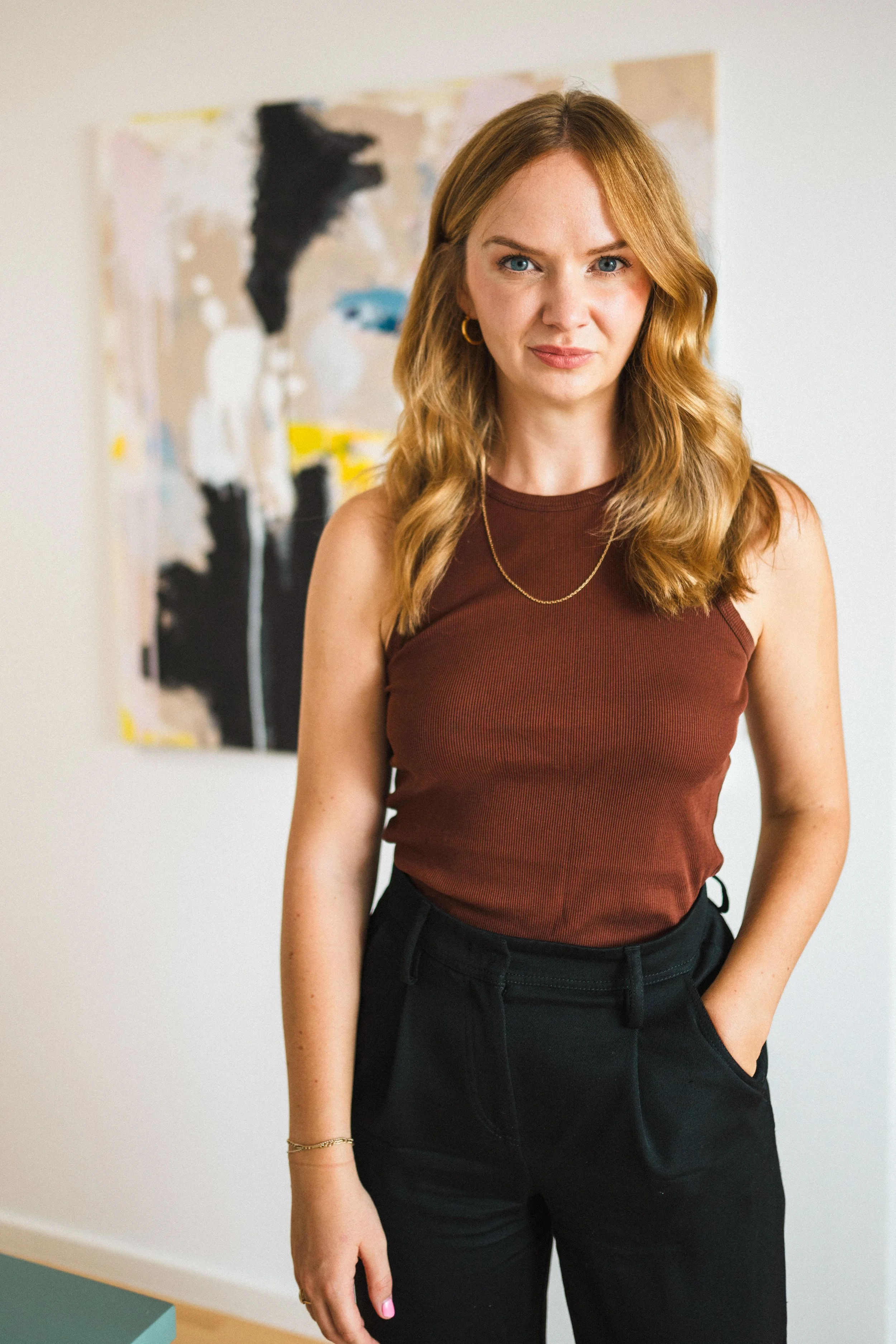 Kristina Lunz stehend in rostrotem Top und schwarzer Hose vor einem Gemälde