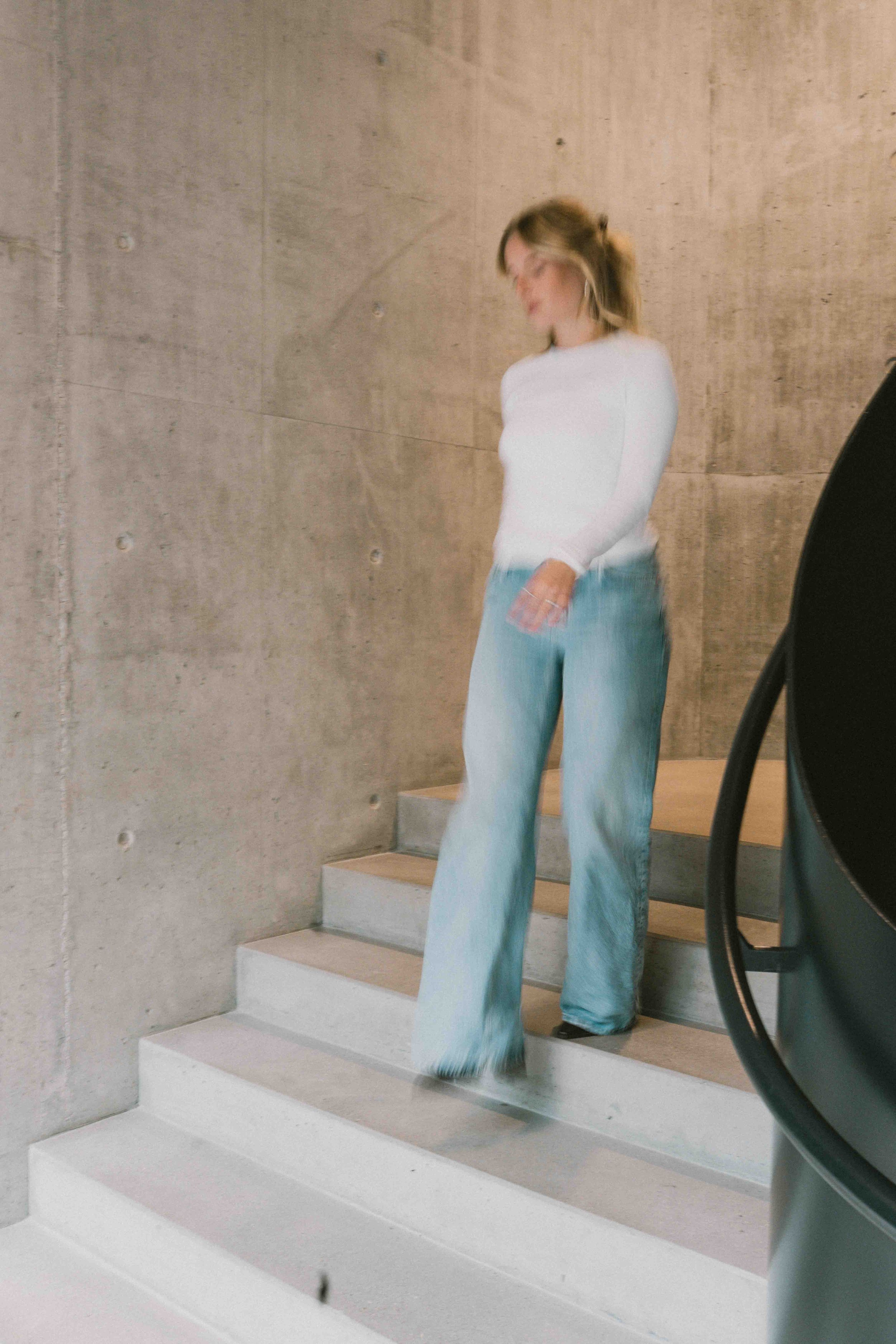 Caro Nowak steht auf einer Steintreppe, weißer Pullover und Jeans
