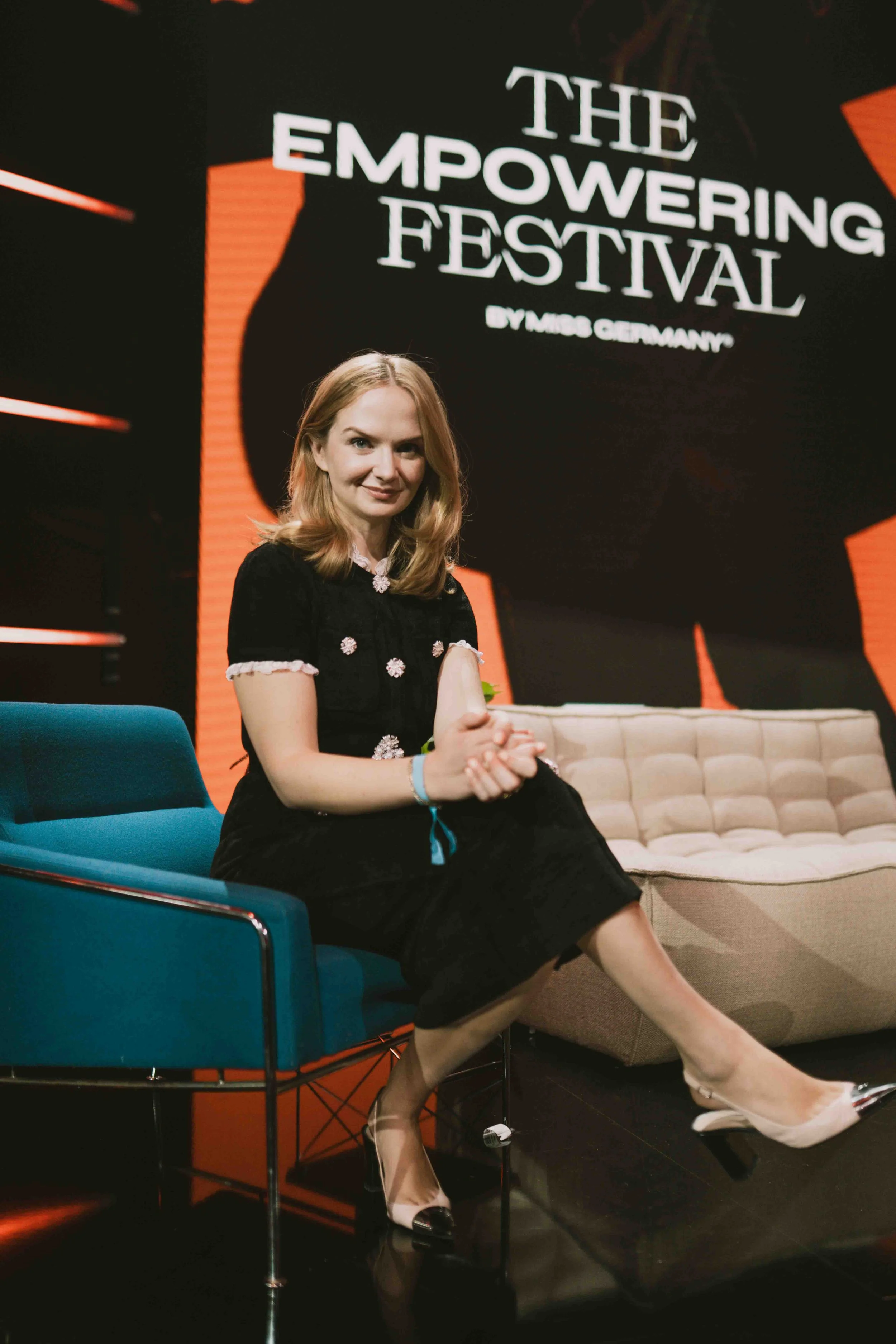 Frau sitzt lächelnd auf einer Bühne vor dem Banner "The Empowering Festival"