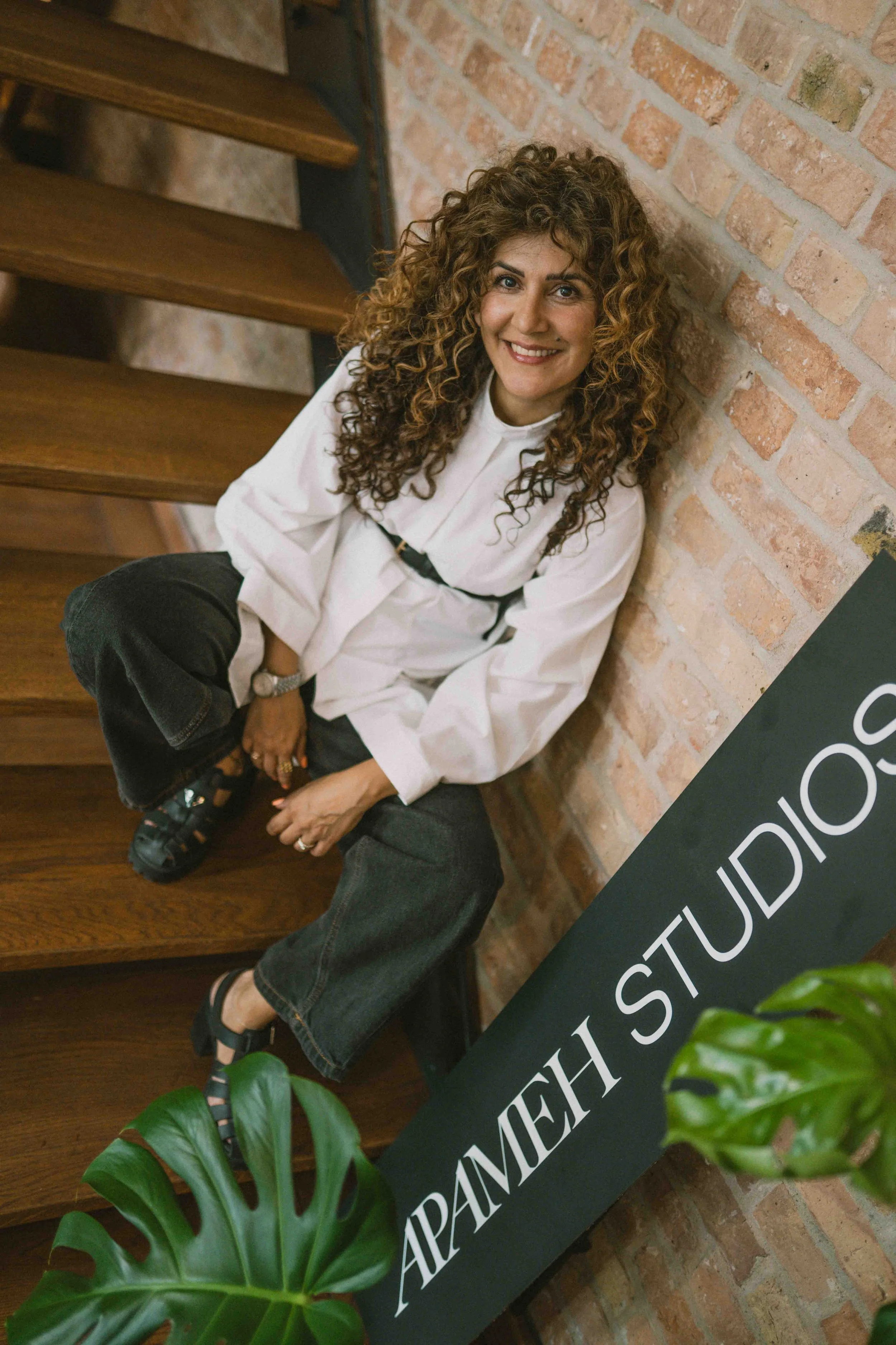 Apameh Schönauer sitzend vor Wand mit "Apameh Studios"-Schriftzug