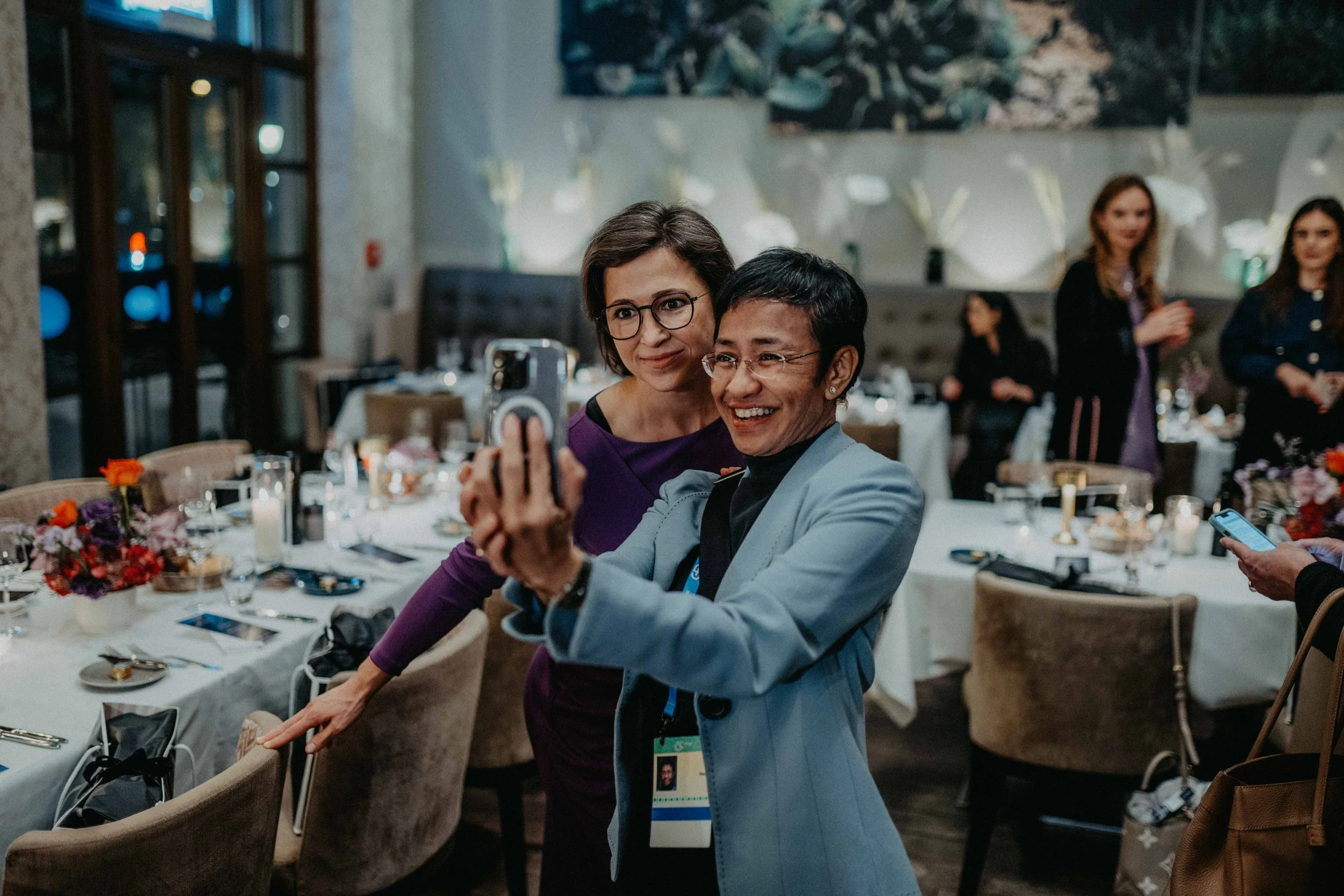 Gruppe von Frauen macht ein Selfie bei einer Abendveranstaltung, im Hintergrund gedeckte Tische
