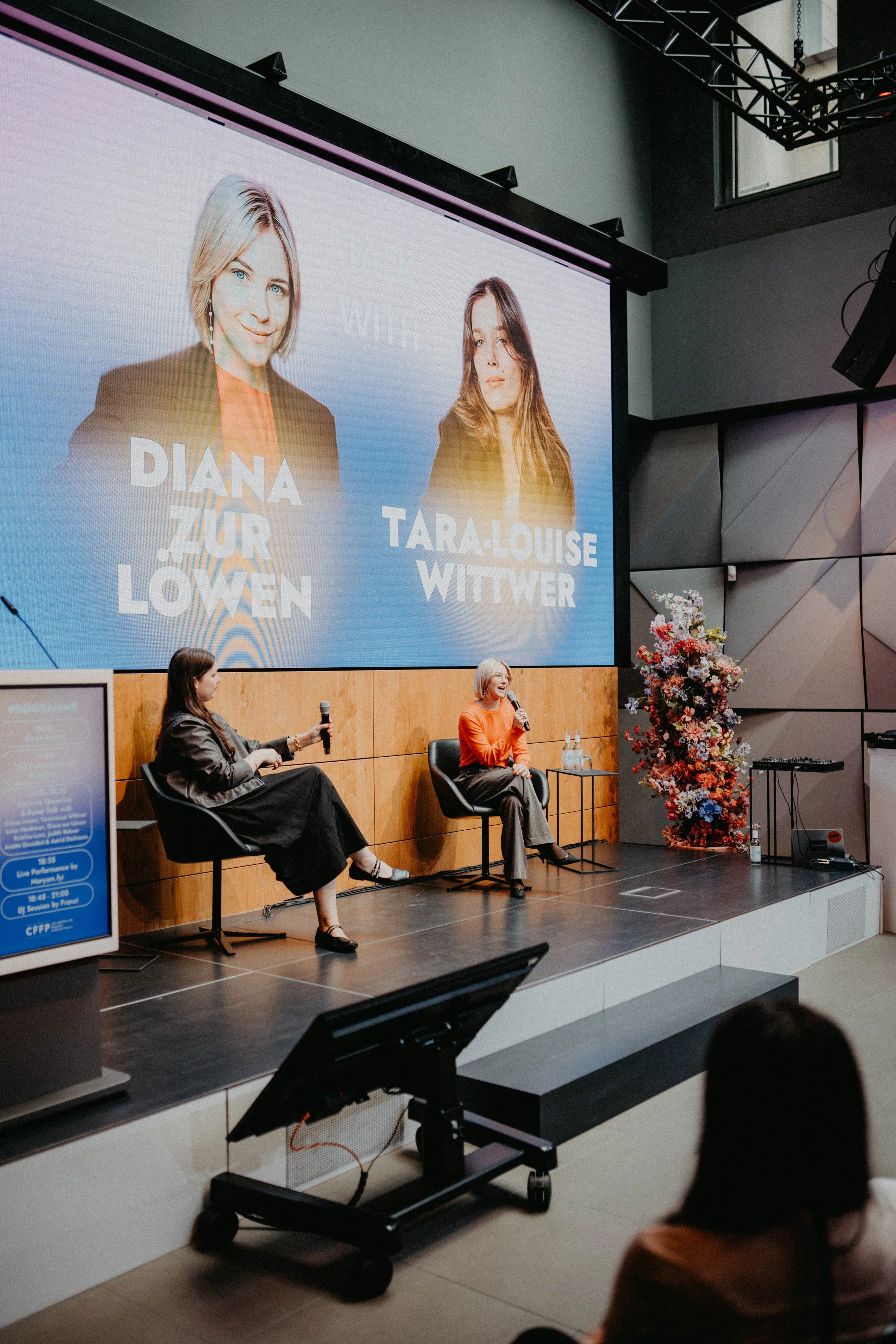 Podiumsdiskussion auf einer Bühne mit großer Leinwand im Hintergrund