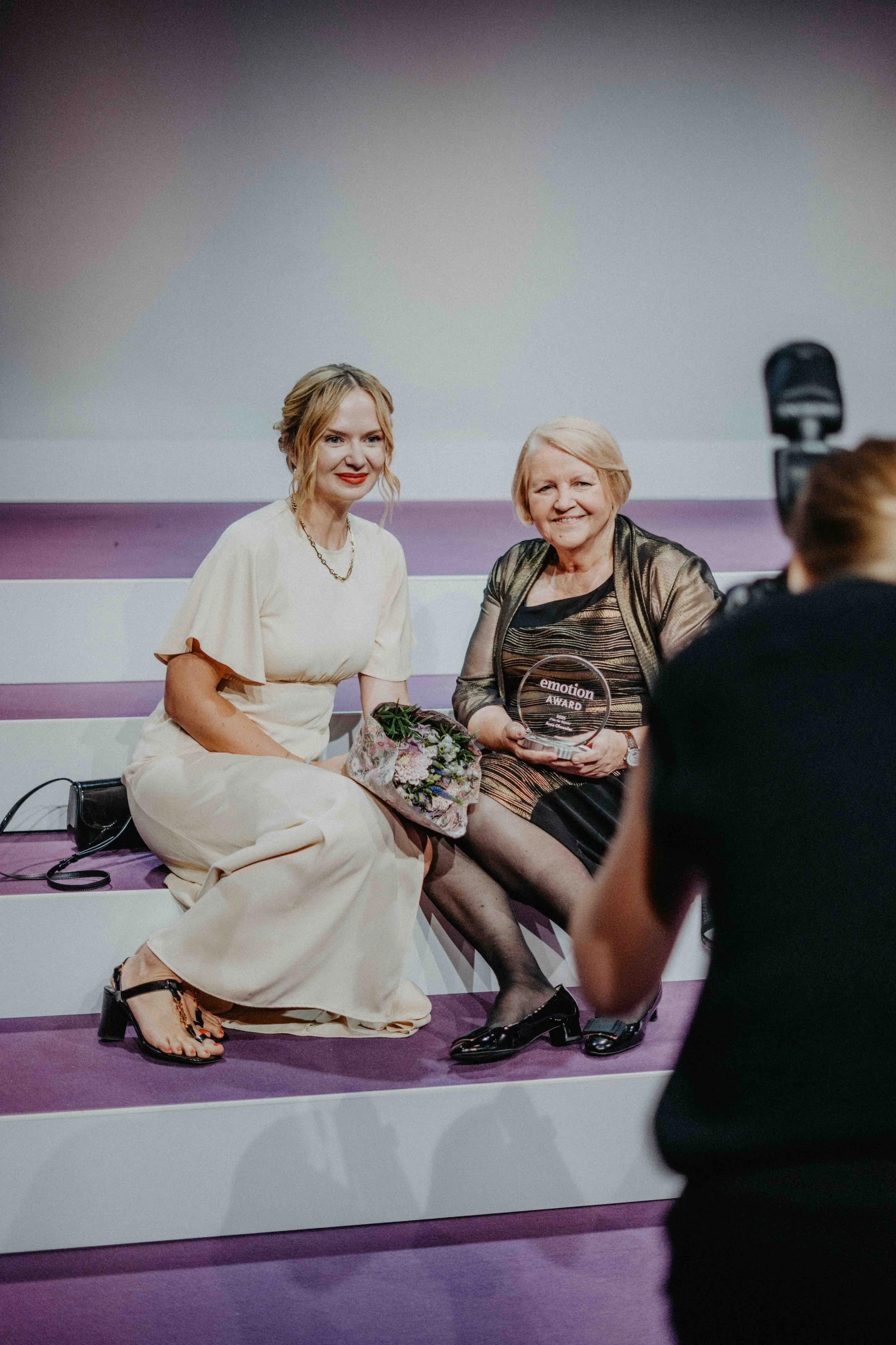 Zwei Frauen sitzen zusammen und werden von einem Fotografen abgelichtet