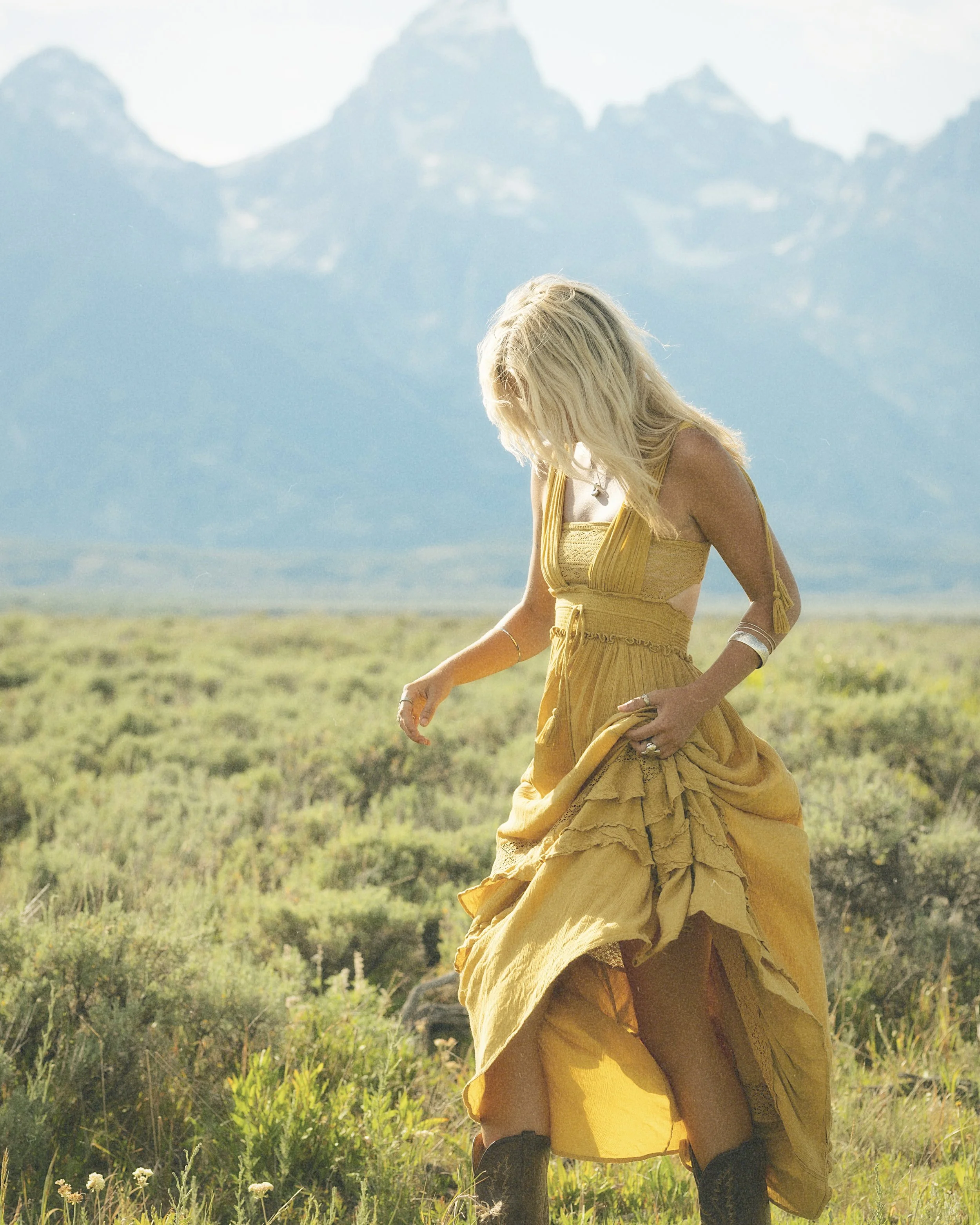 A woman in a yellow dress walking through a flower field in Grand Teton National Park.