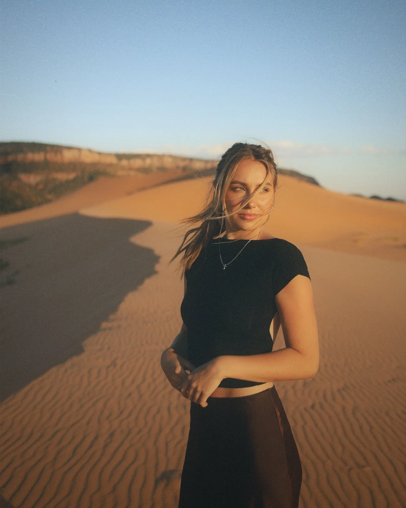 A woman posing at golden hour in sand dunes.