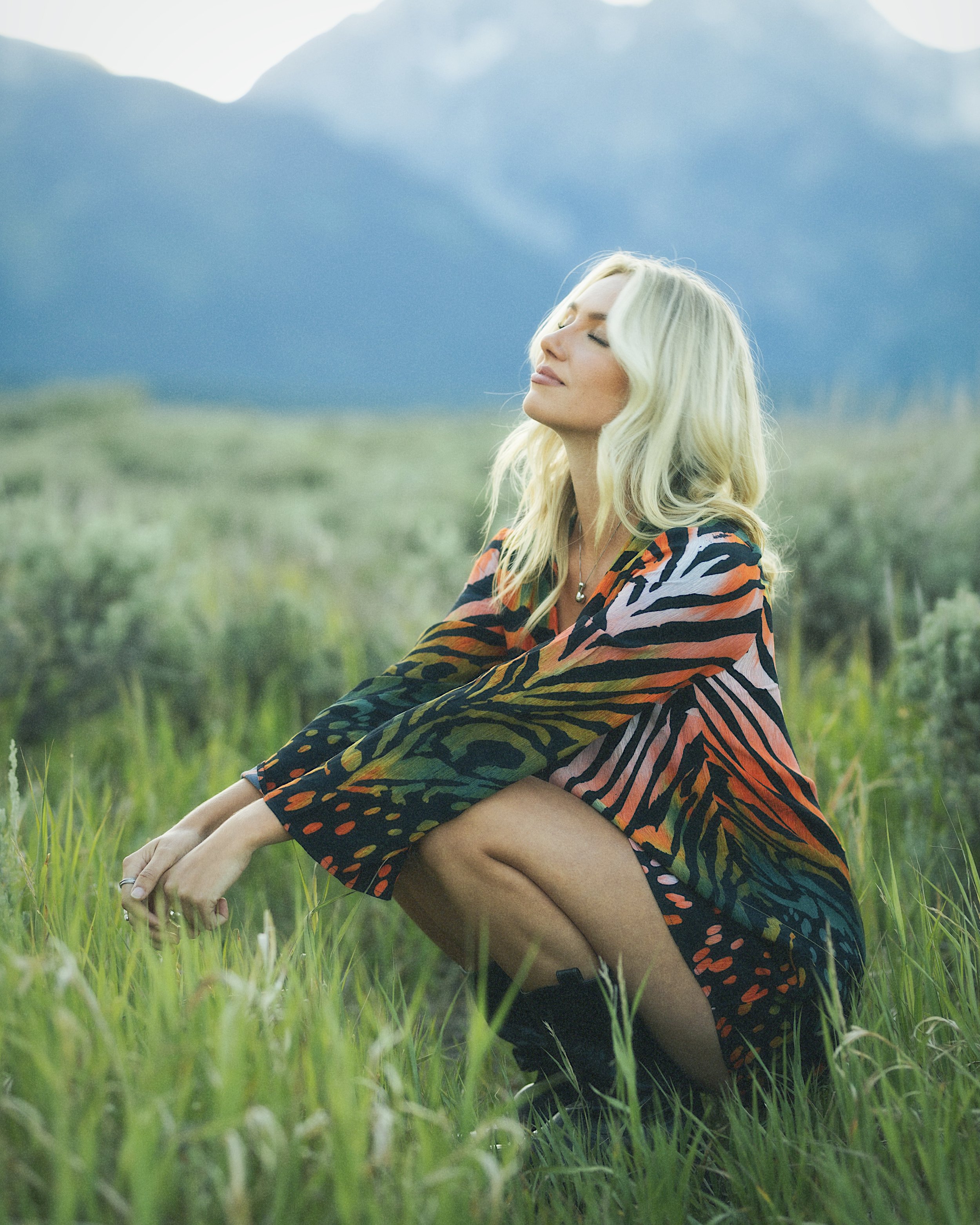A woman in a colorful outfit posing in front of the Grand Teton Mountain range in Wyoming.