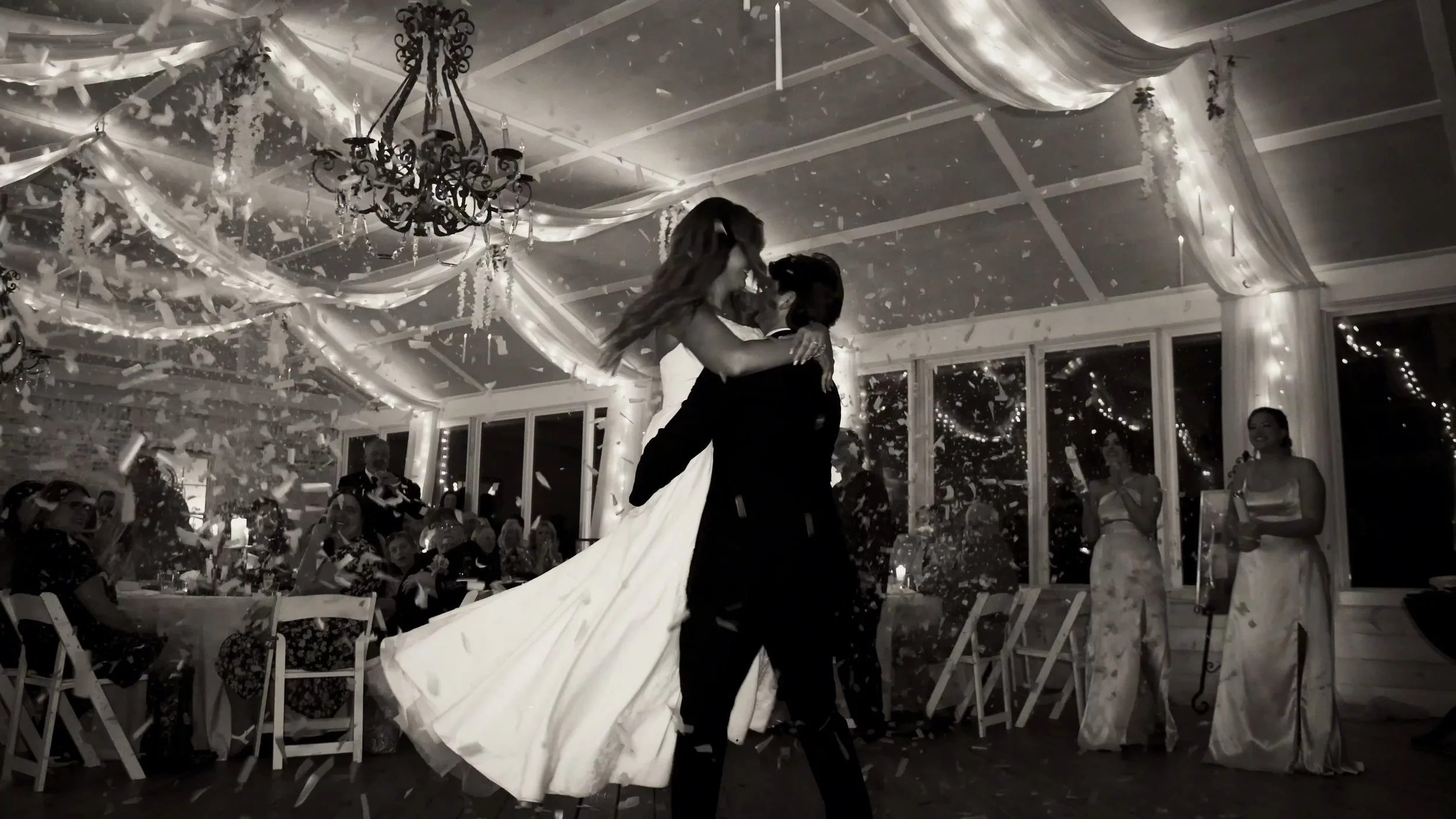 A groom spinning his bride around while confetti is being sprayed around them in the room.