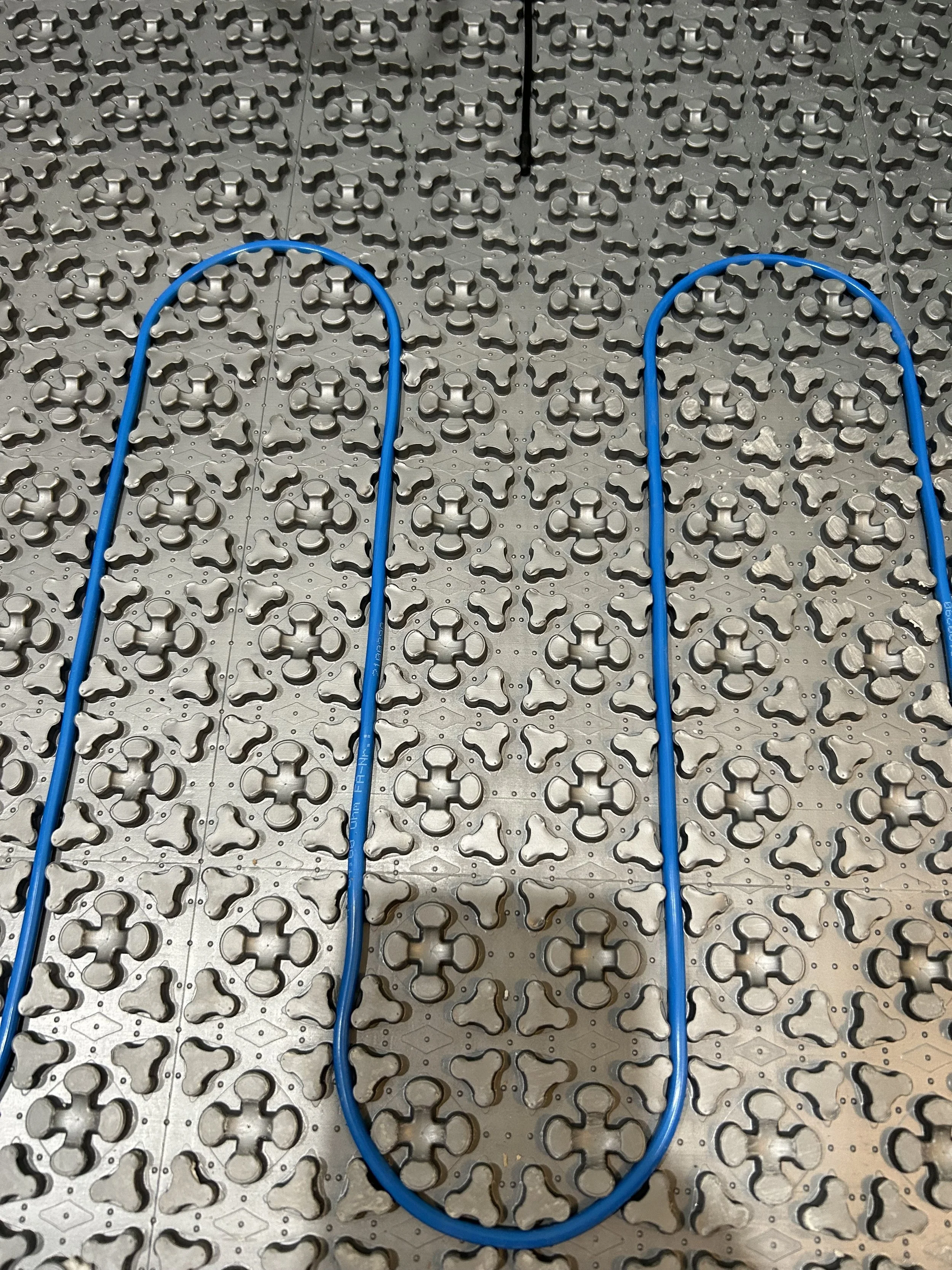 Two blue jumper cables are placed on a metal floor with a pattern of raised circular and cross-shaped designs.