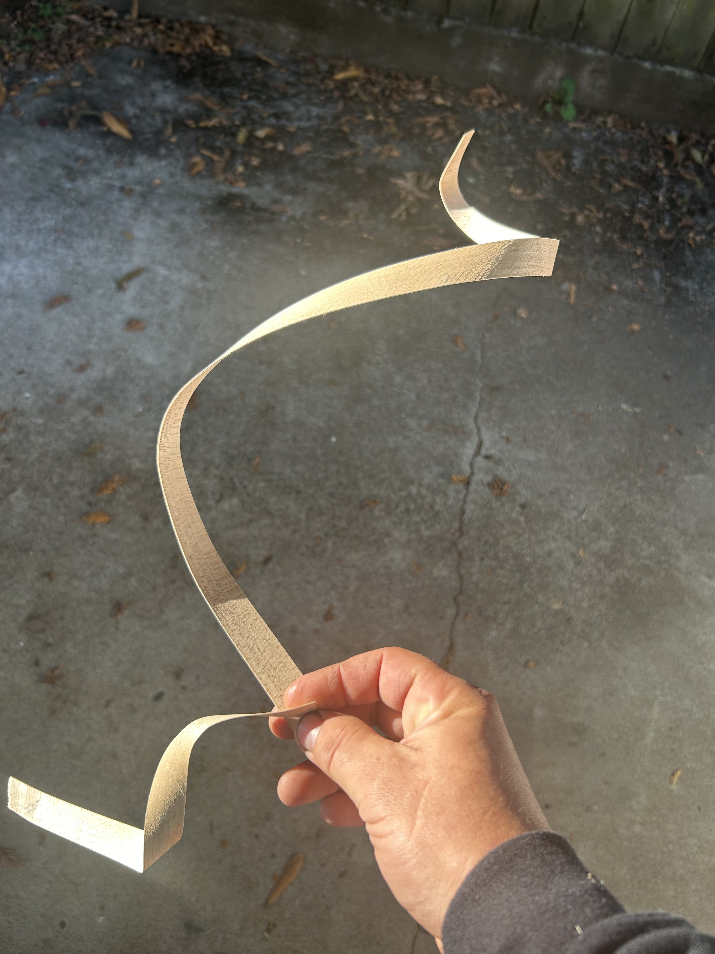 Person holding a wooden or cardboard spiral sculpture outdoors on concrete ground.