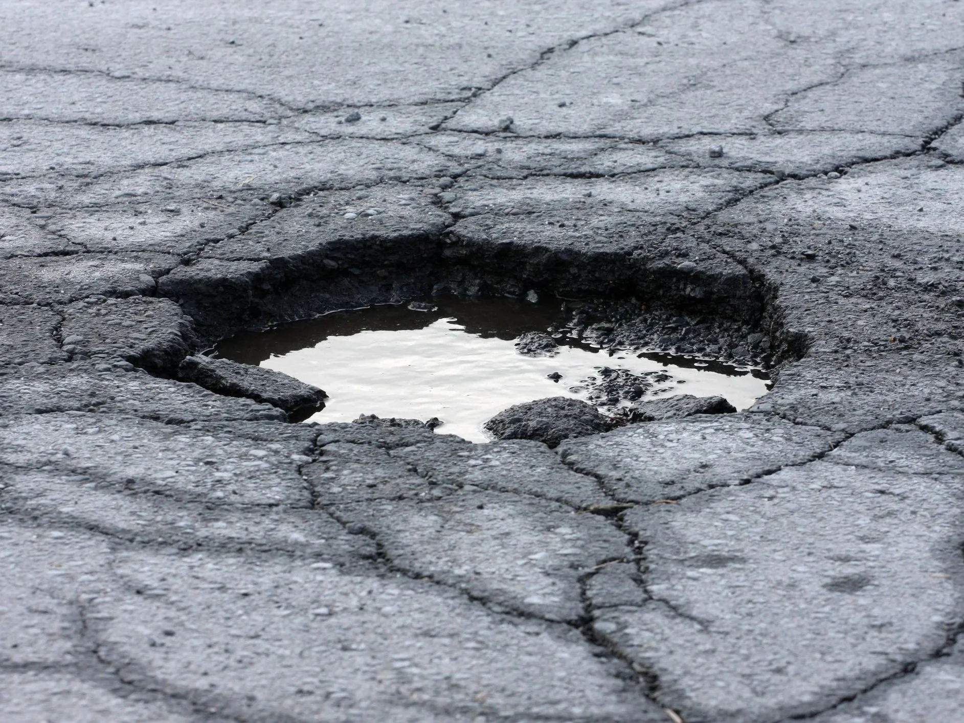 Close-up of cracked asphalt with a pothole filled with rainwater.