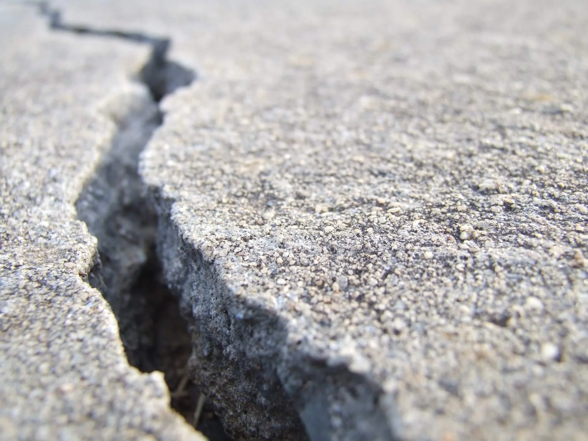 Close-up of a cracked concrete surface with a deep fissure.