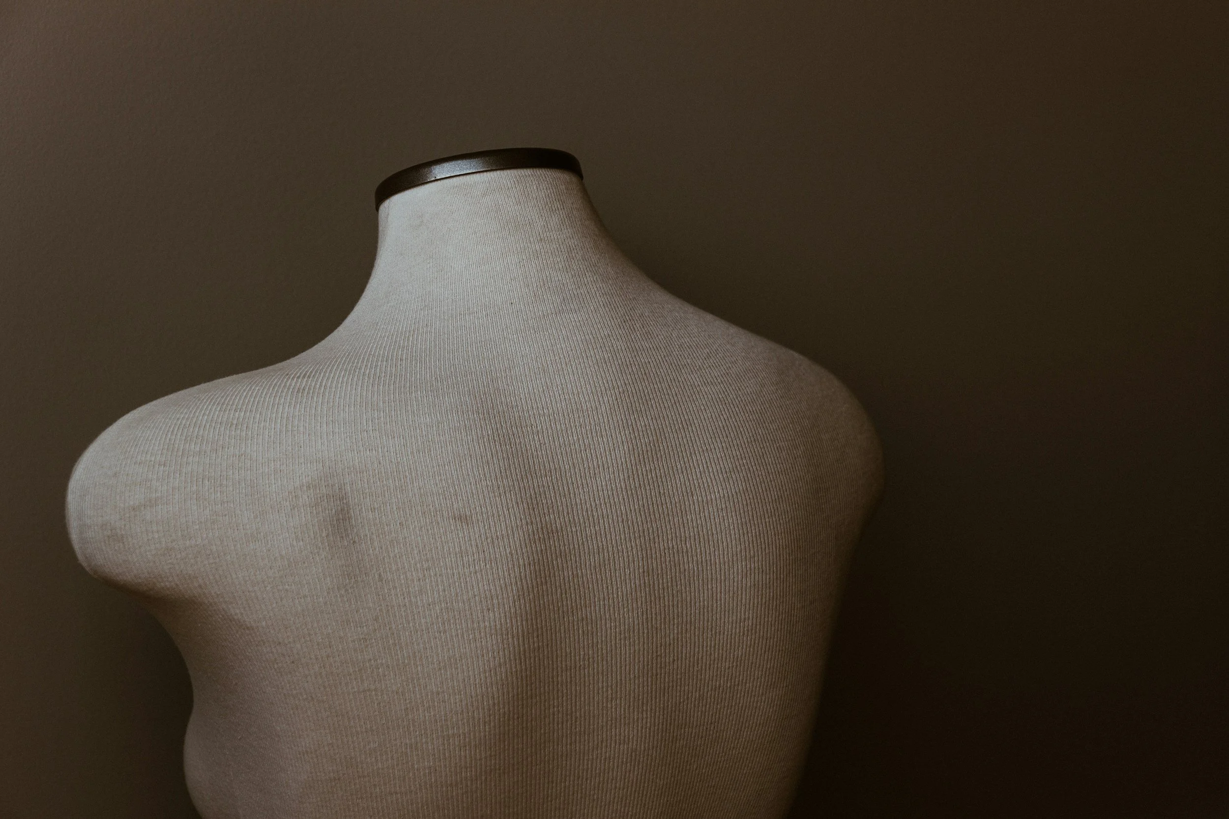 A beige fabric-covered dress form or mannequin against a dark background.