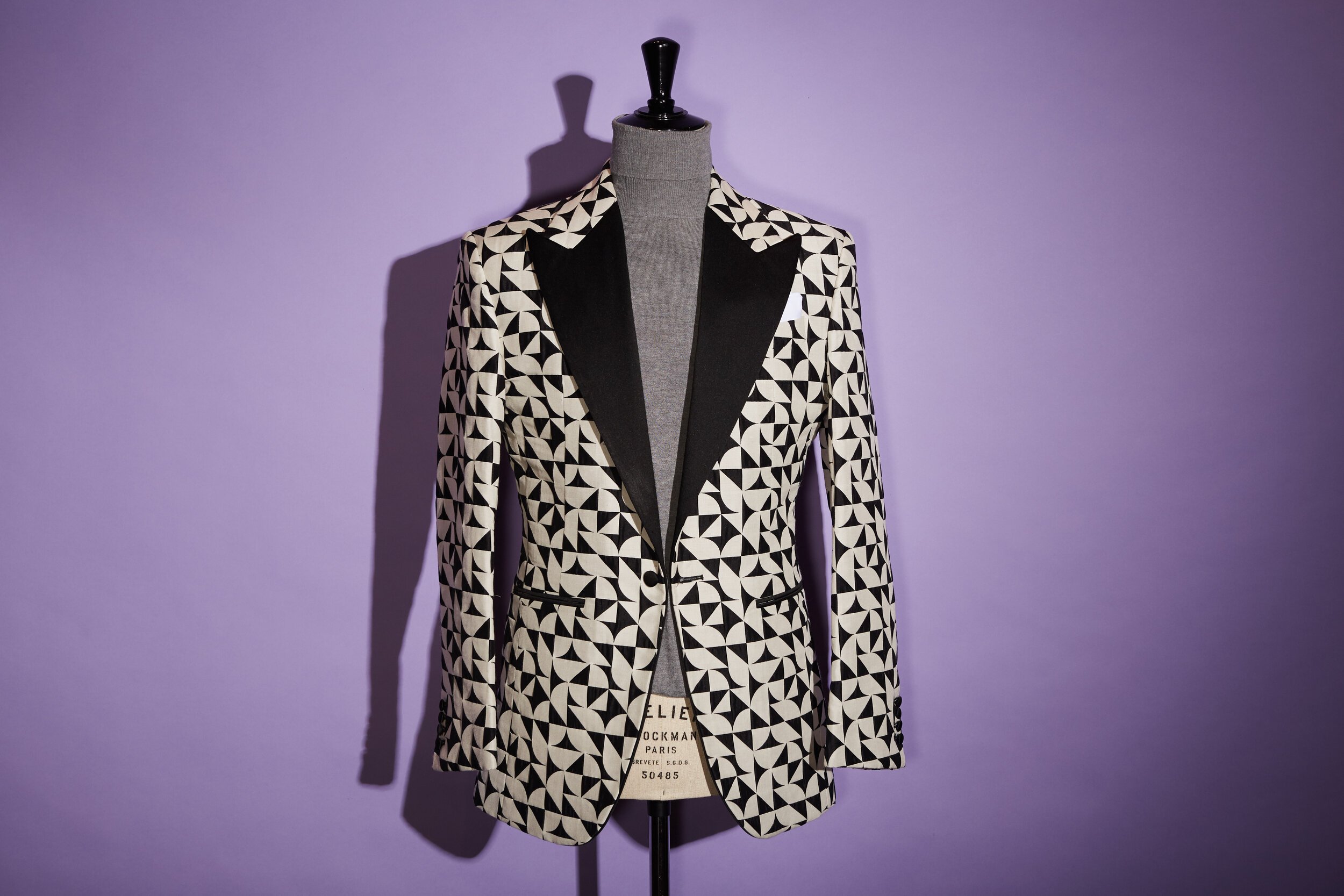 A mannequin wearing a black and white geometric patterned blazer against a purple background.