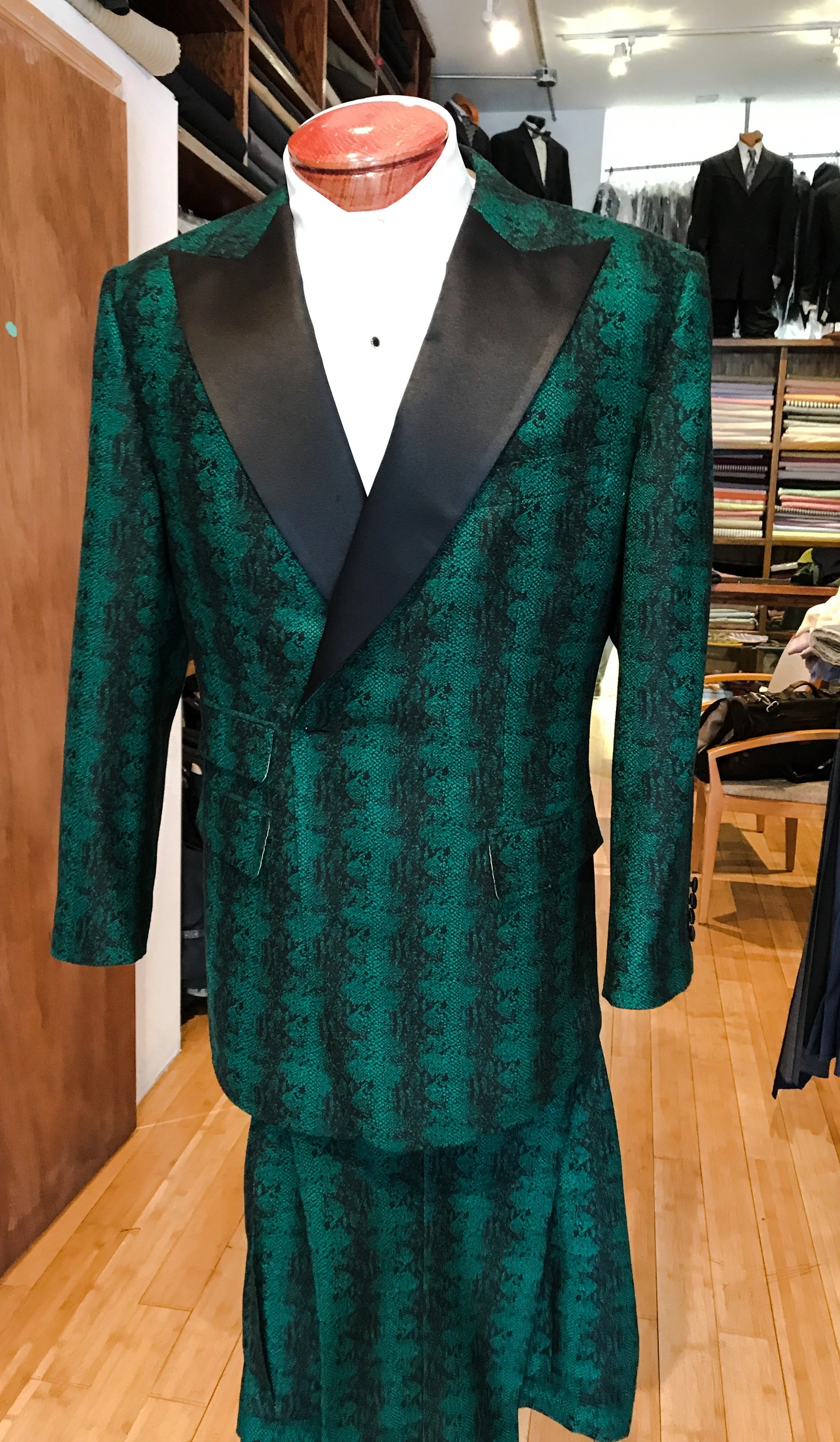 Mannequin dressed in a green and black patterned tuxedo with a satin lapel and a white shirt, in a clothing store.
