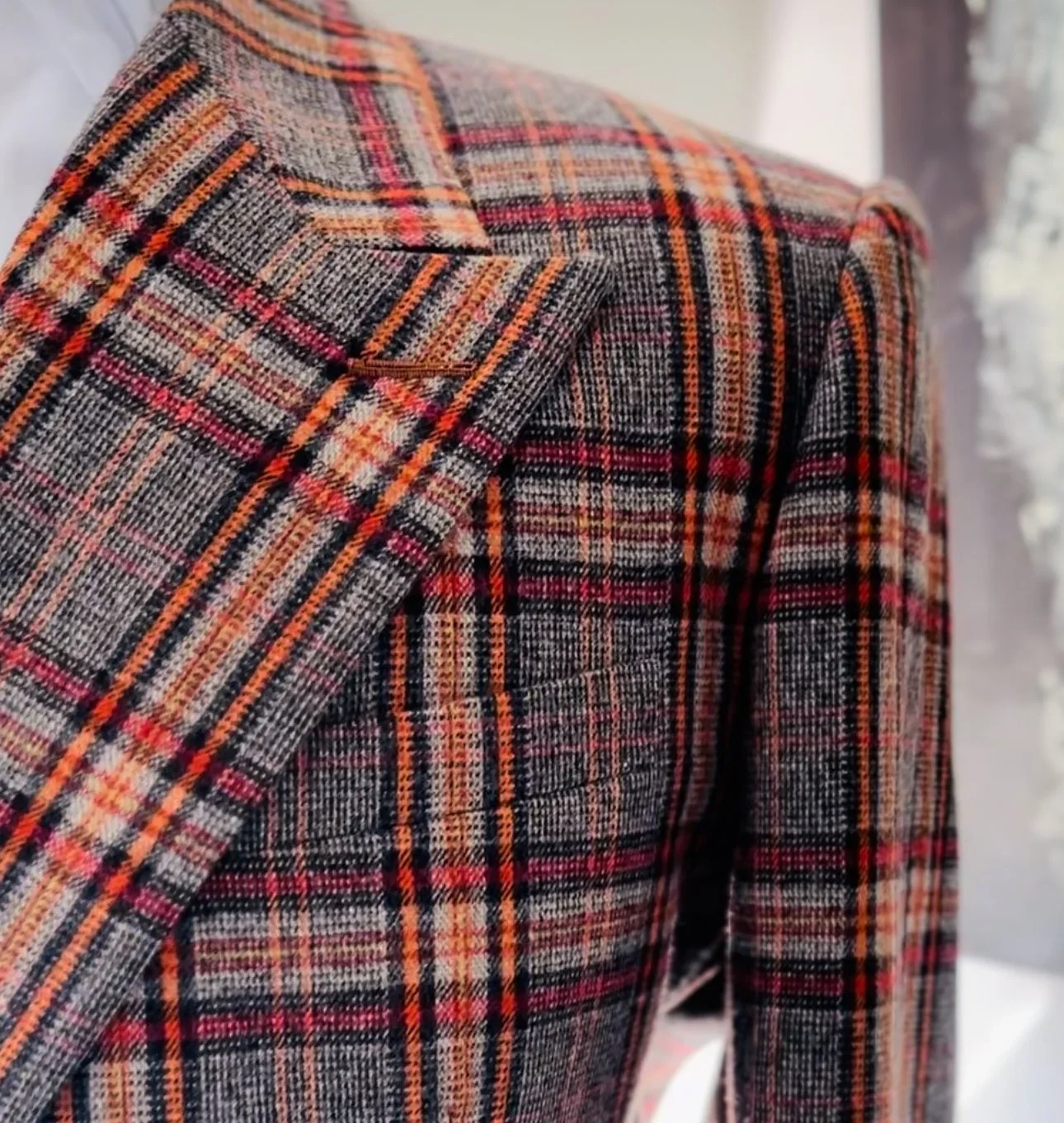 Close-up of a plaid blazer with grey, red, orange, and black patterns on a mannequin.