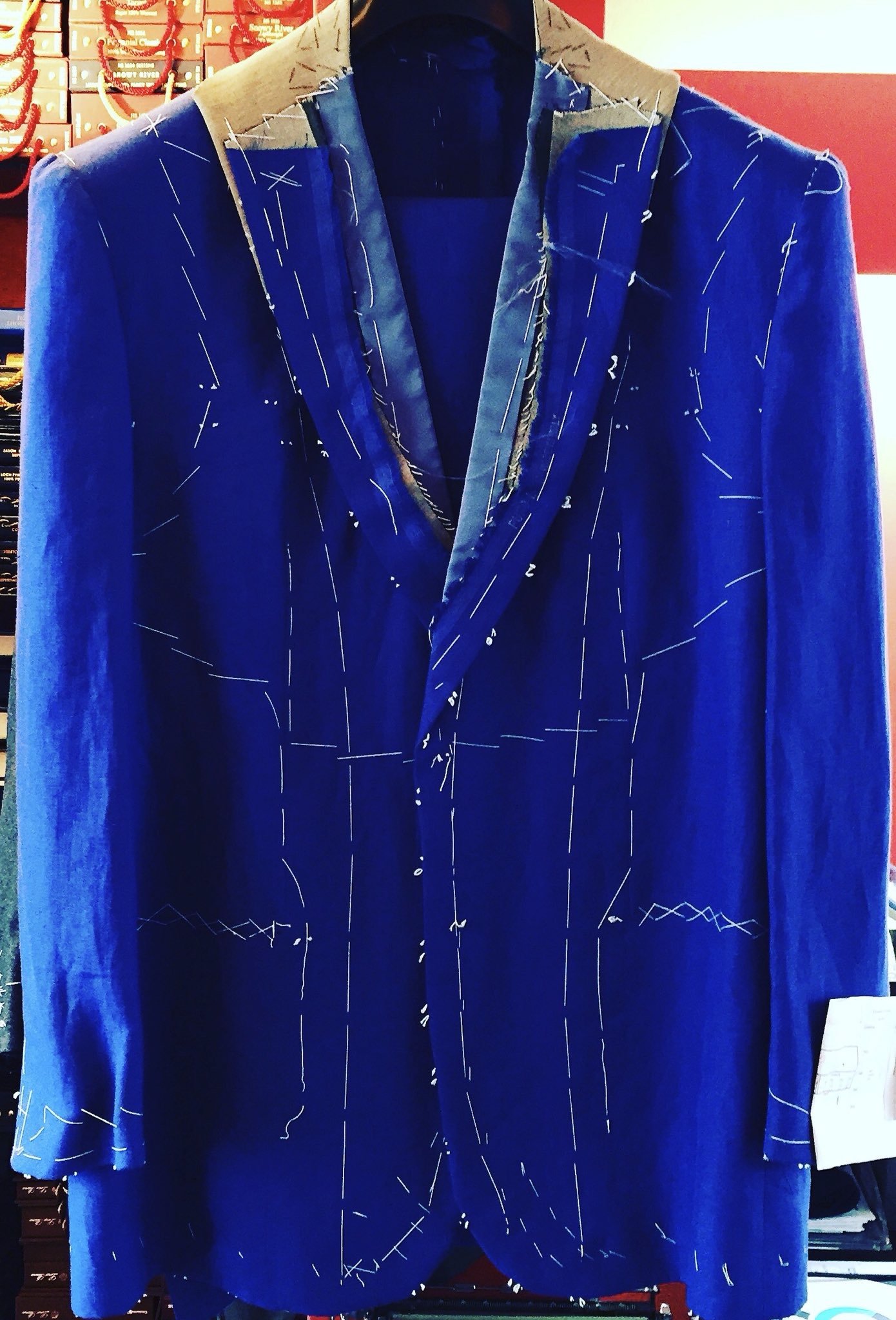 A blue suit jacket hanging on a wooden hanger. The jacket has white stitched lines resembling a star chart or constellation pattern.
