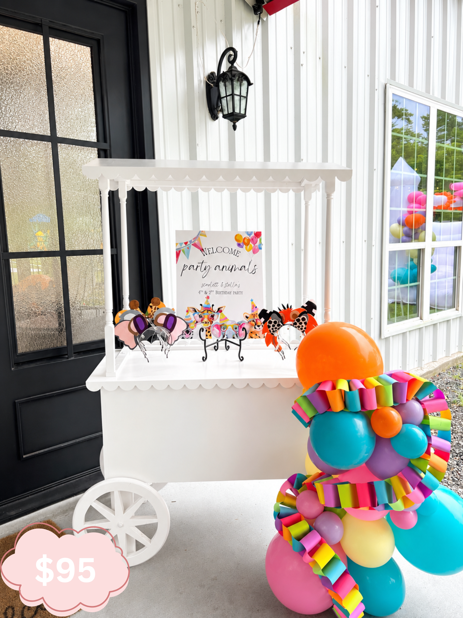 Colorful balloon bouquet and a white cart with a sign that says 'Welcome party animals' and features illustrations of animals at a birthday party, with a large orange balloon in the foreground and decorations for a celebration.