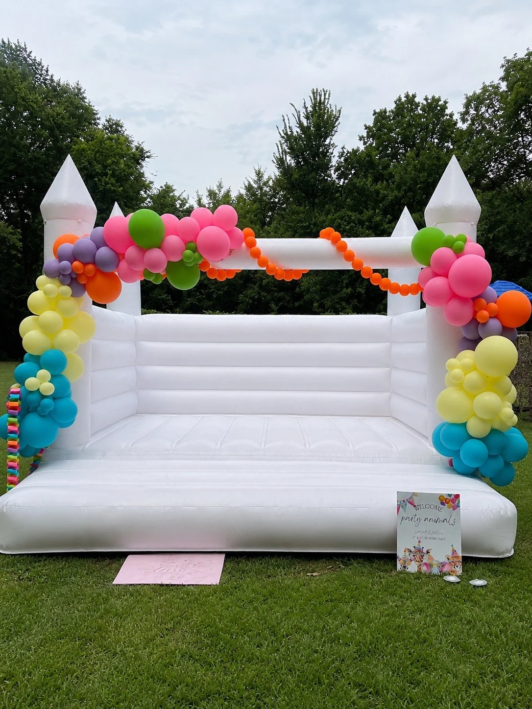 Inflatable bounce house decorated with colorful balloons and a welcoming sign for a party.