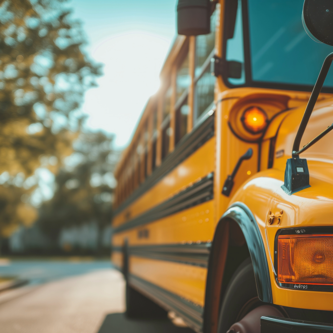 Close-up of a yellow school bus with an illuminated indicator light, parked outdoors with trees in the background.