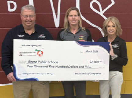 Three people standing in front of a red and yellow wall holding an oversized check for $2,500 made out to Reese Public Schools, dated March 2023.