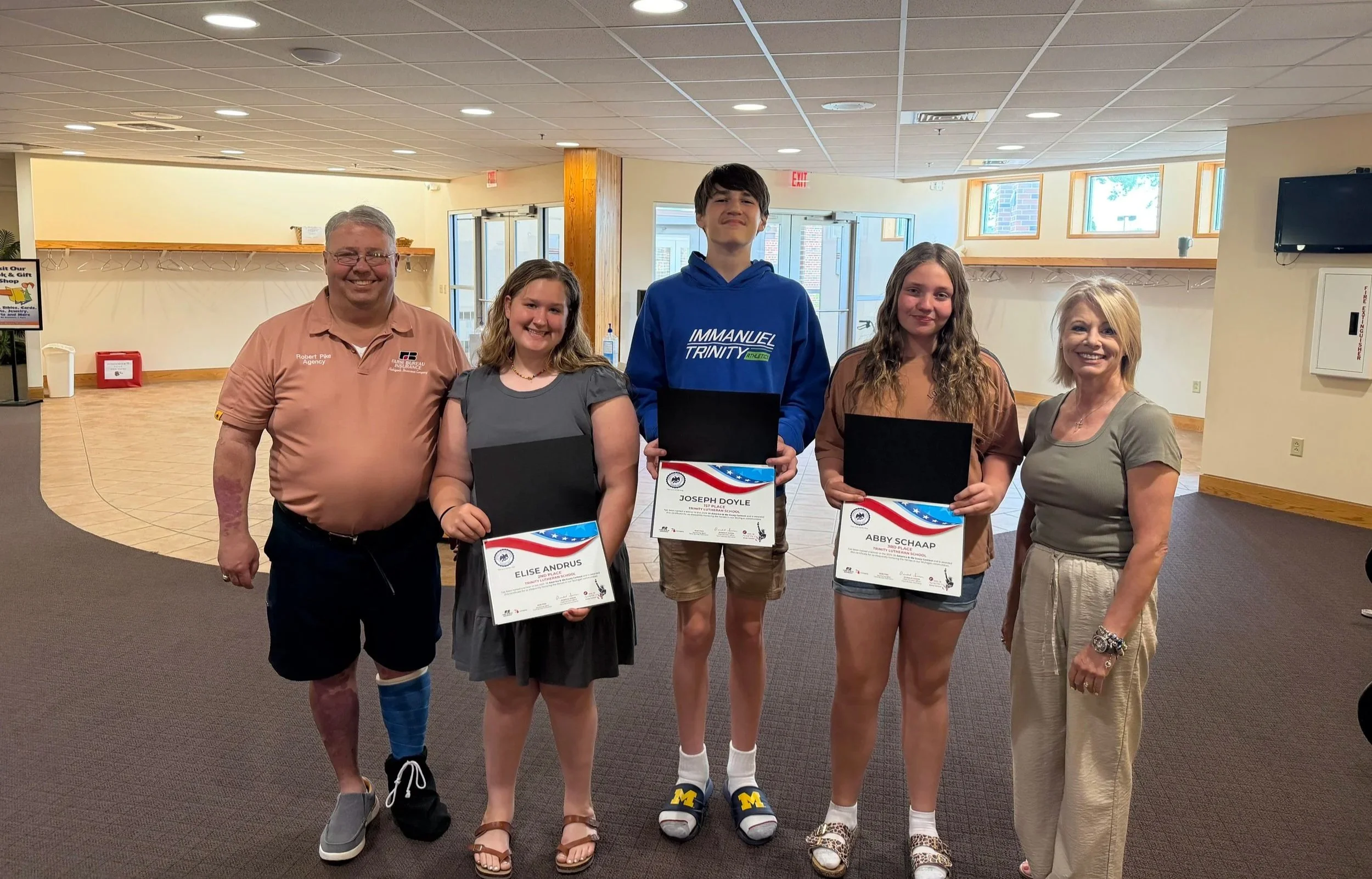 A group of five people standing indoors, holding certificates, and smiling at the camera.