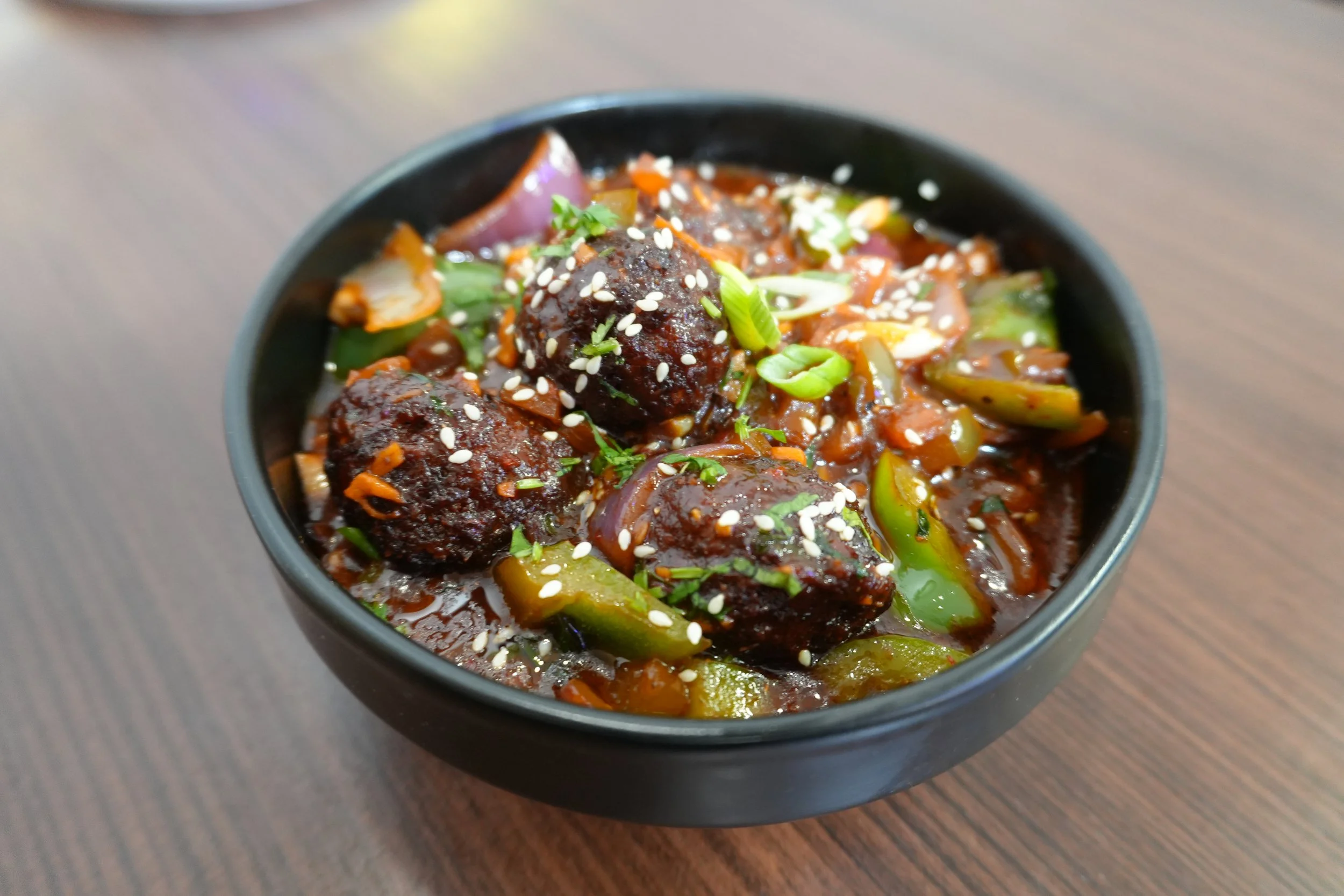 A bowl of Asian-style meatballs in dark sauce with chopped green onions and sesame seeds