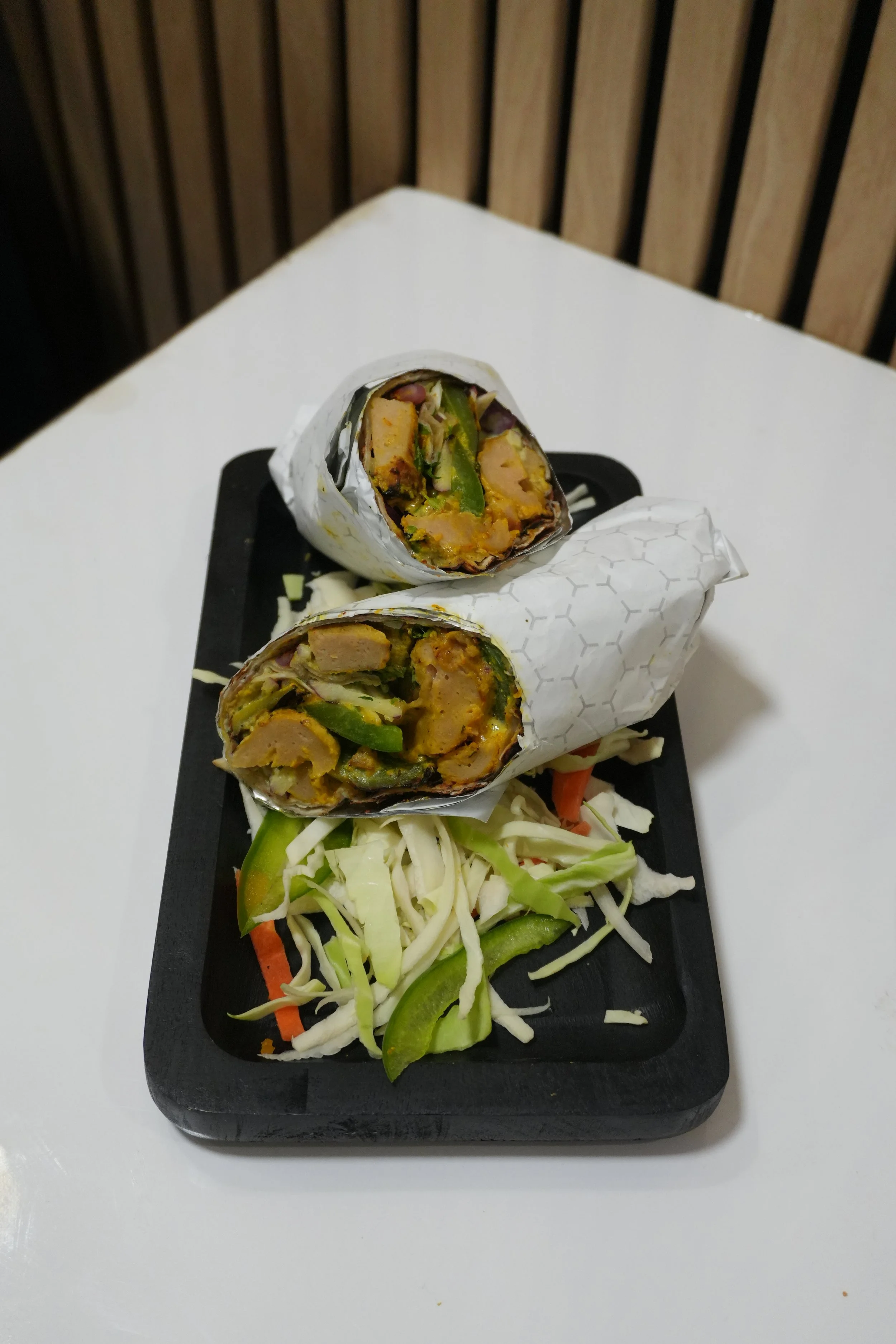 Two burritos cut open on a black tray with shredded cabbage and sliced green peppers.