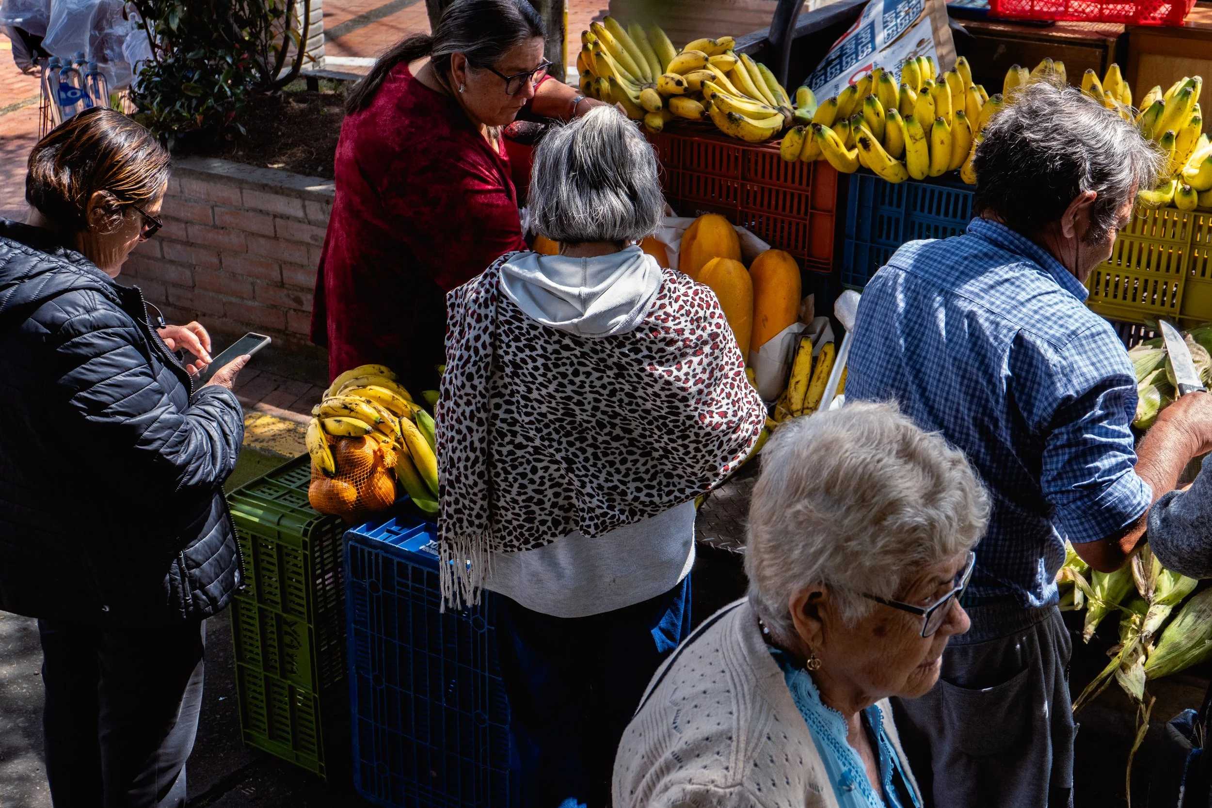 People shopping at a fruit stand with bananas and melons in an outdoor market.