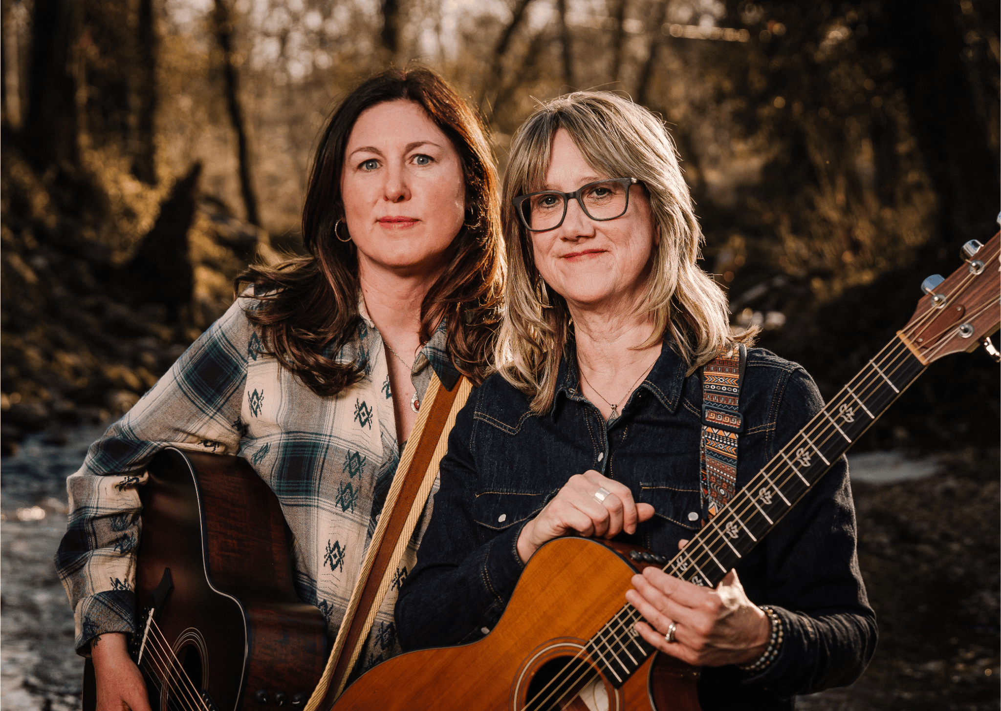 Two women holding guitars outdoors during sunset