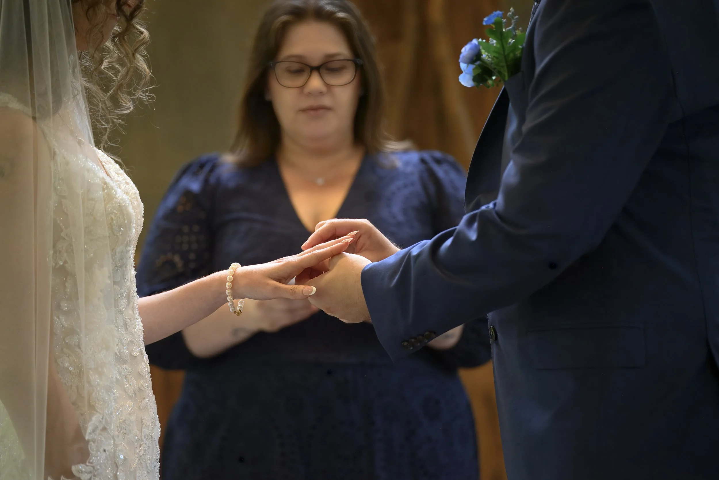 A couple exchanging wedding rings during a ceremony, with an officiant overseeing the event.
