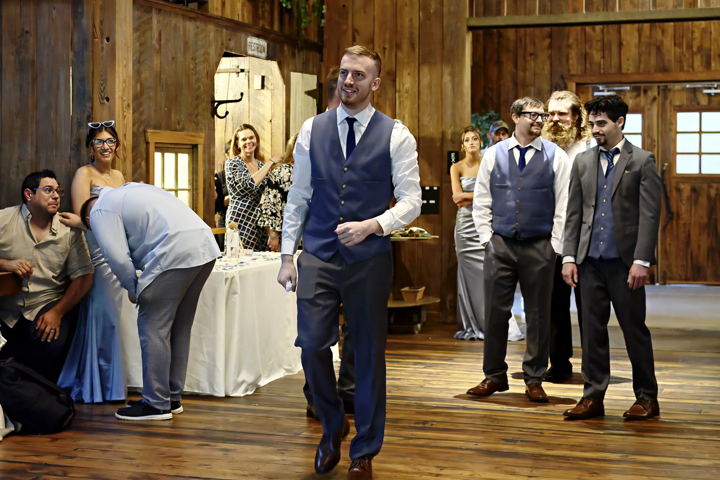Group of people dressed in formal attire at a wedding or event inside a wooden venue.