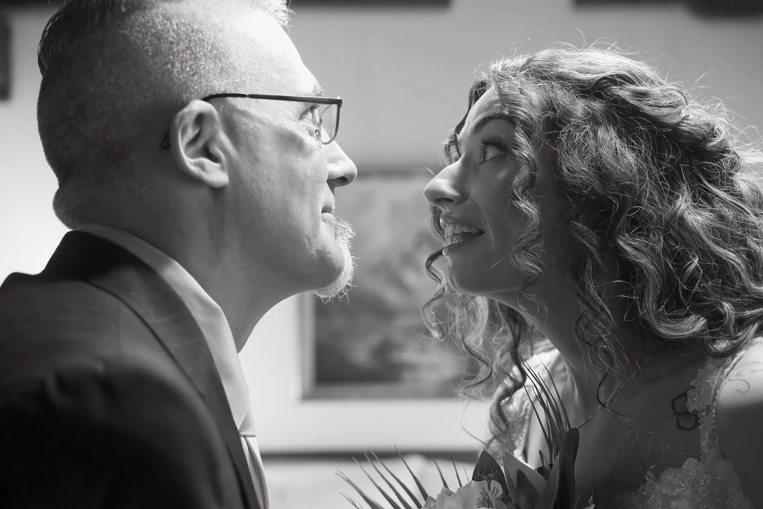 Black and white close-up of a man and a woman facing each other, smiling and looking into each other's eyes, in what appears to be a joyful moment.