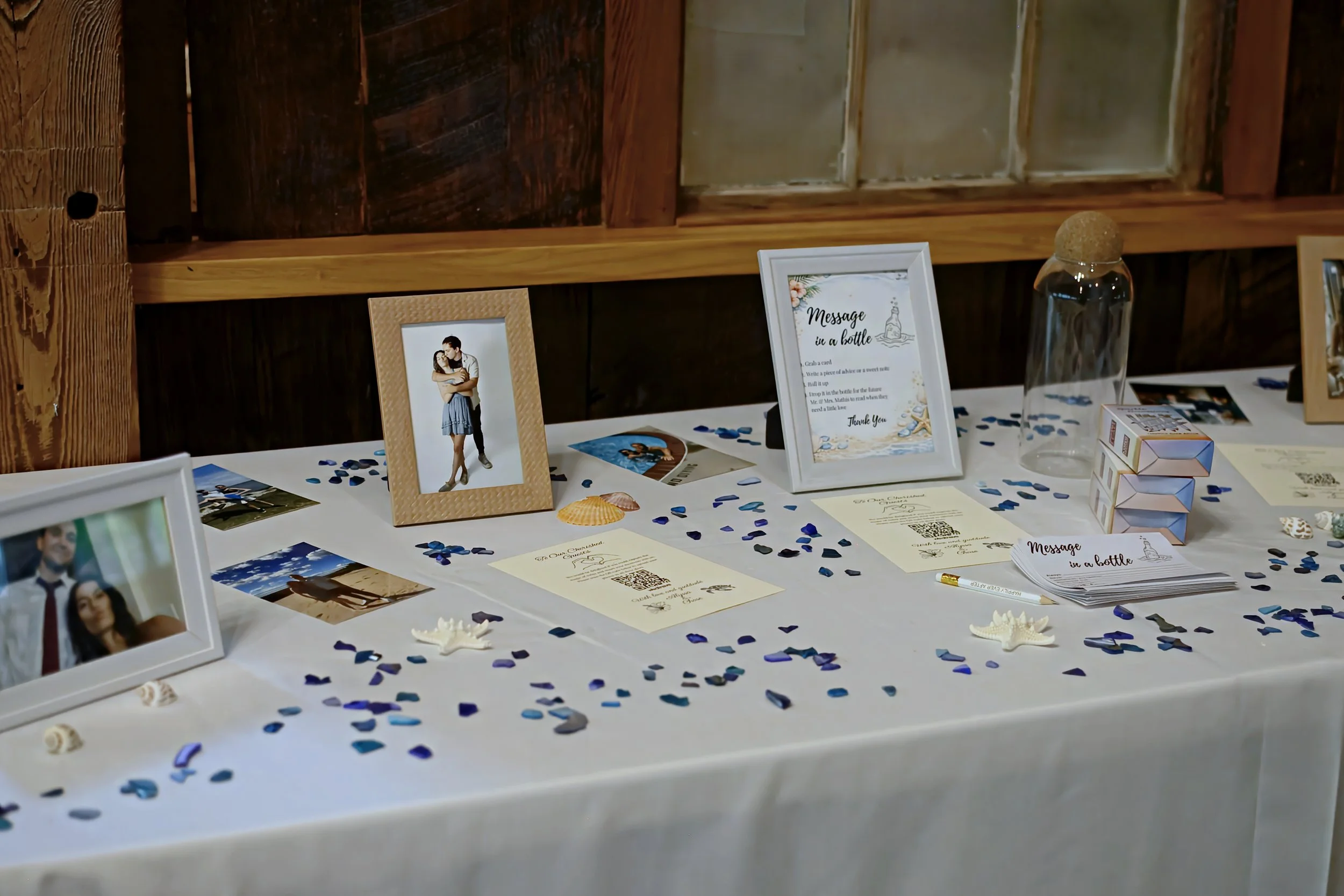 A table decorated with seashells, blue confetti, framed photographs, and a sign that reads 'Message in a bottle.'