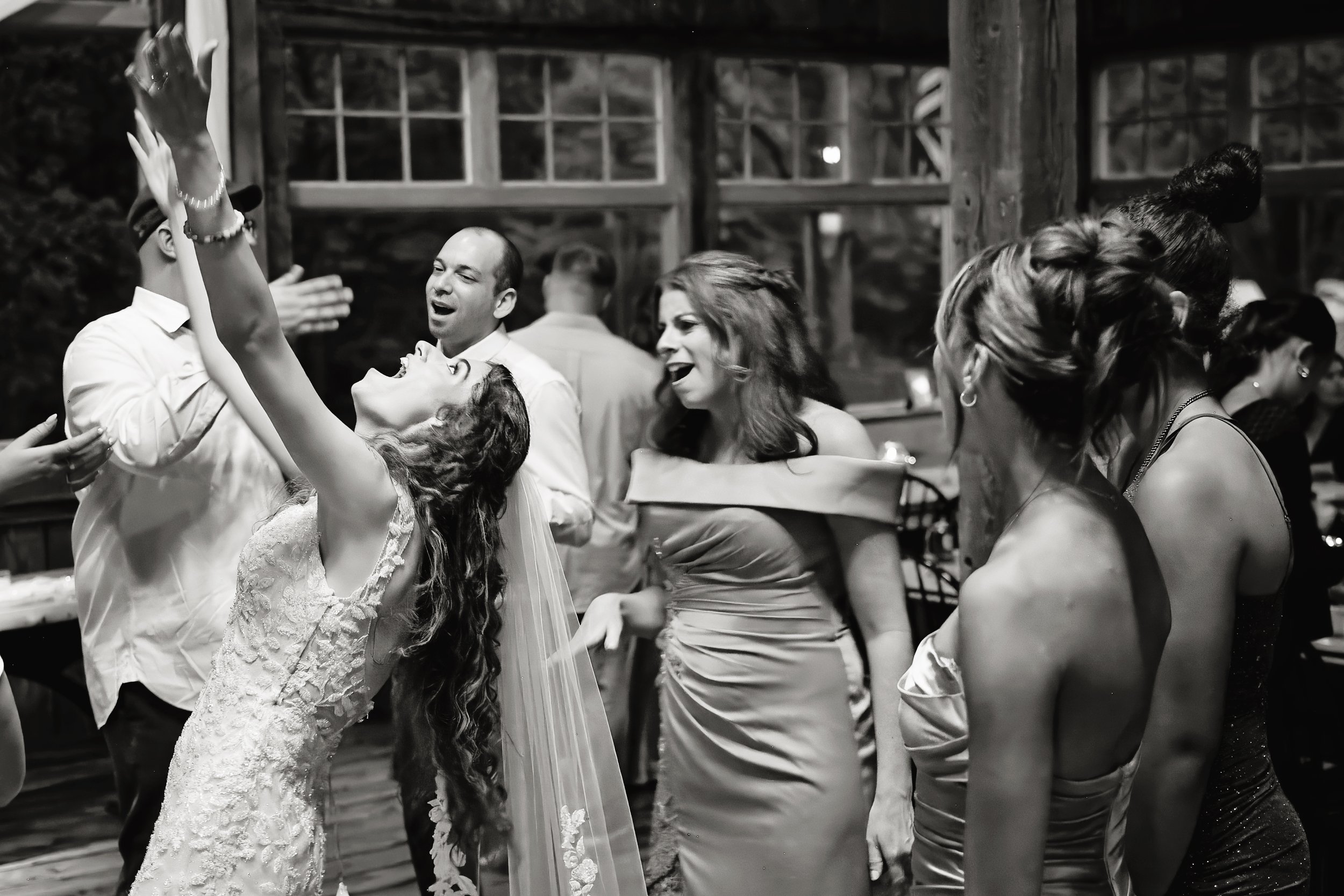 People dancing and celebrating at a party, with a woman in a wedding dress dancing with her arms raised, and others smiling and enjoying the moment.