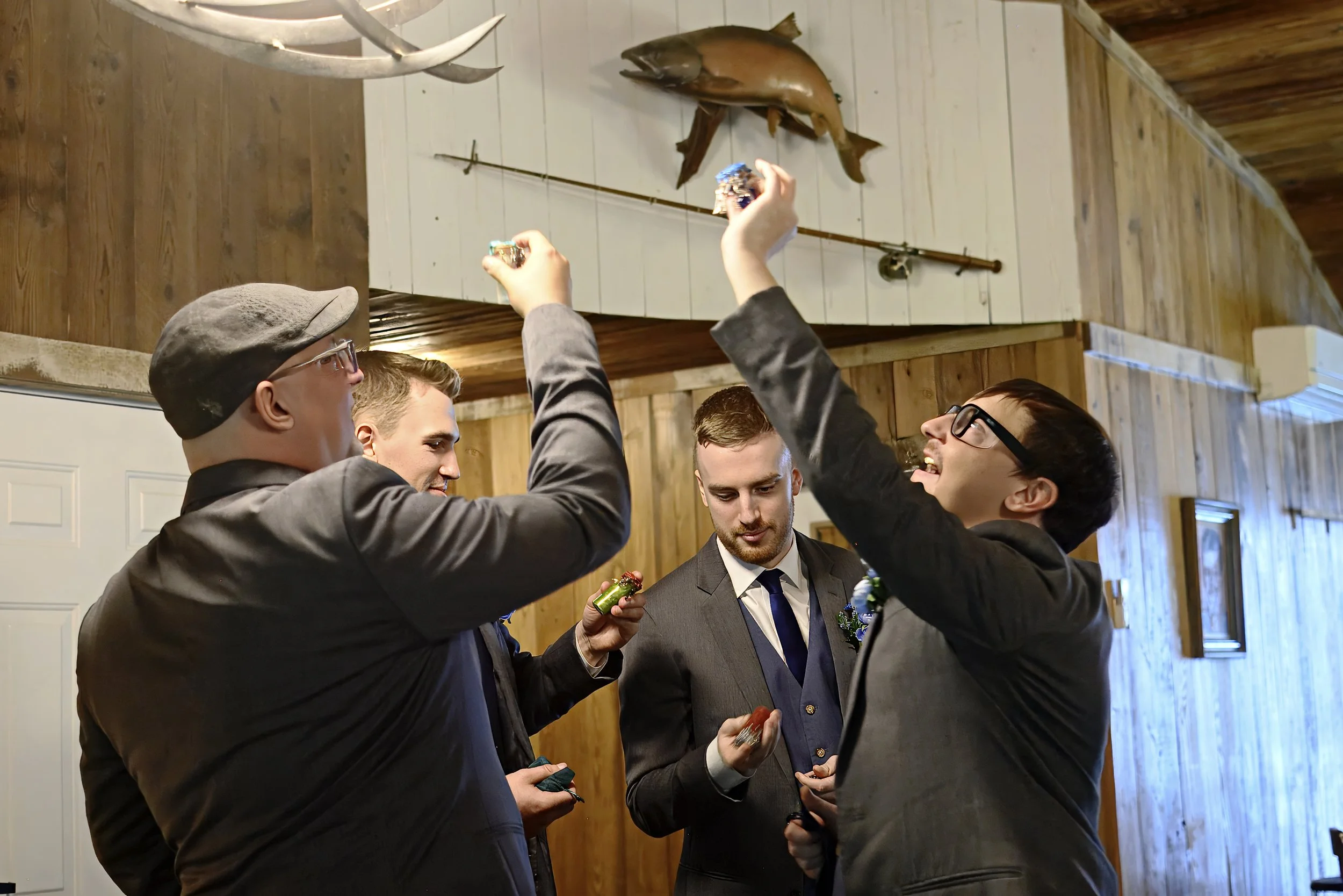 Group of men in formal attire smiling and exchanging gifts inside a rustic wooden room, with a mounted fish and antlers on the wall in the background.