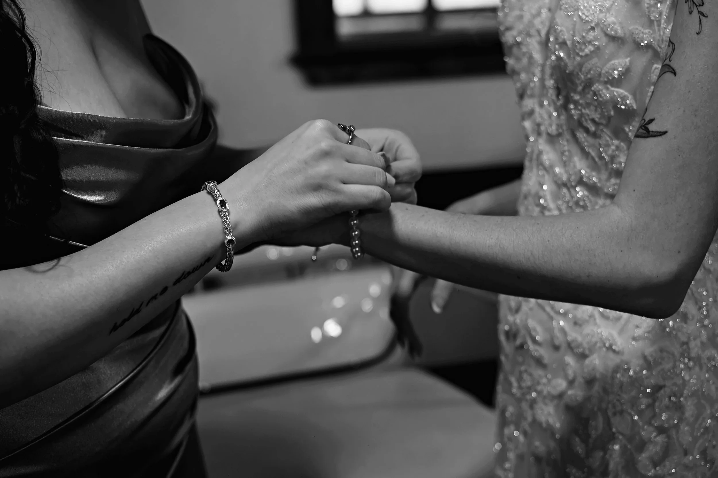 Black and white photo of a person wearing jewelry and a fancy dress, holding hands with another person dressed in a sparkling evening gown.