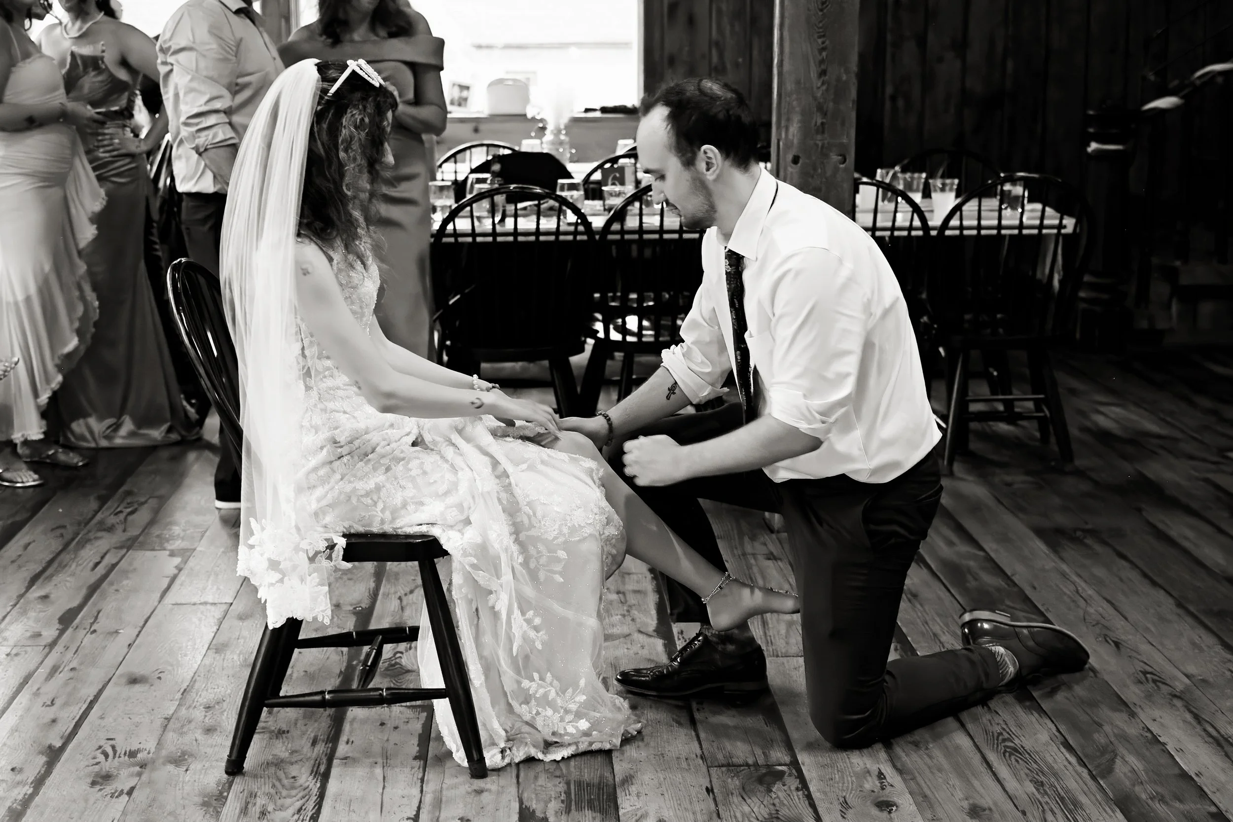 A man on one knee holding a woman's hand and proposing marriage during a wedding ceremony, with wedding guests in the background.