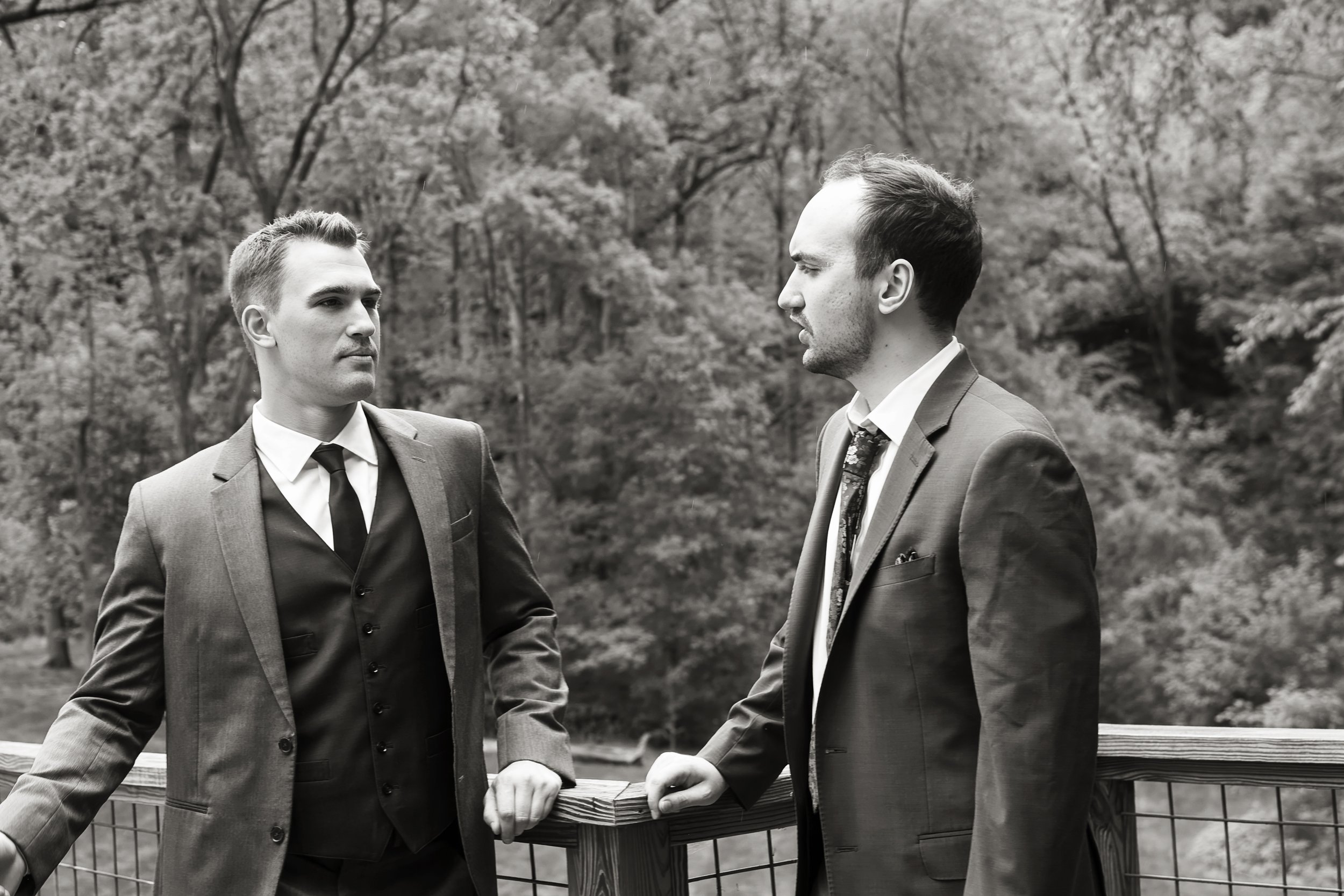 Two men in suits having a conversation outdoors in a park with trees in the background, in black and white.