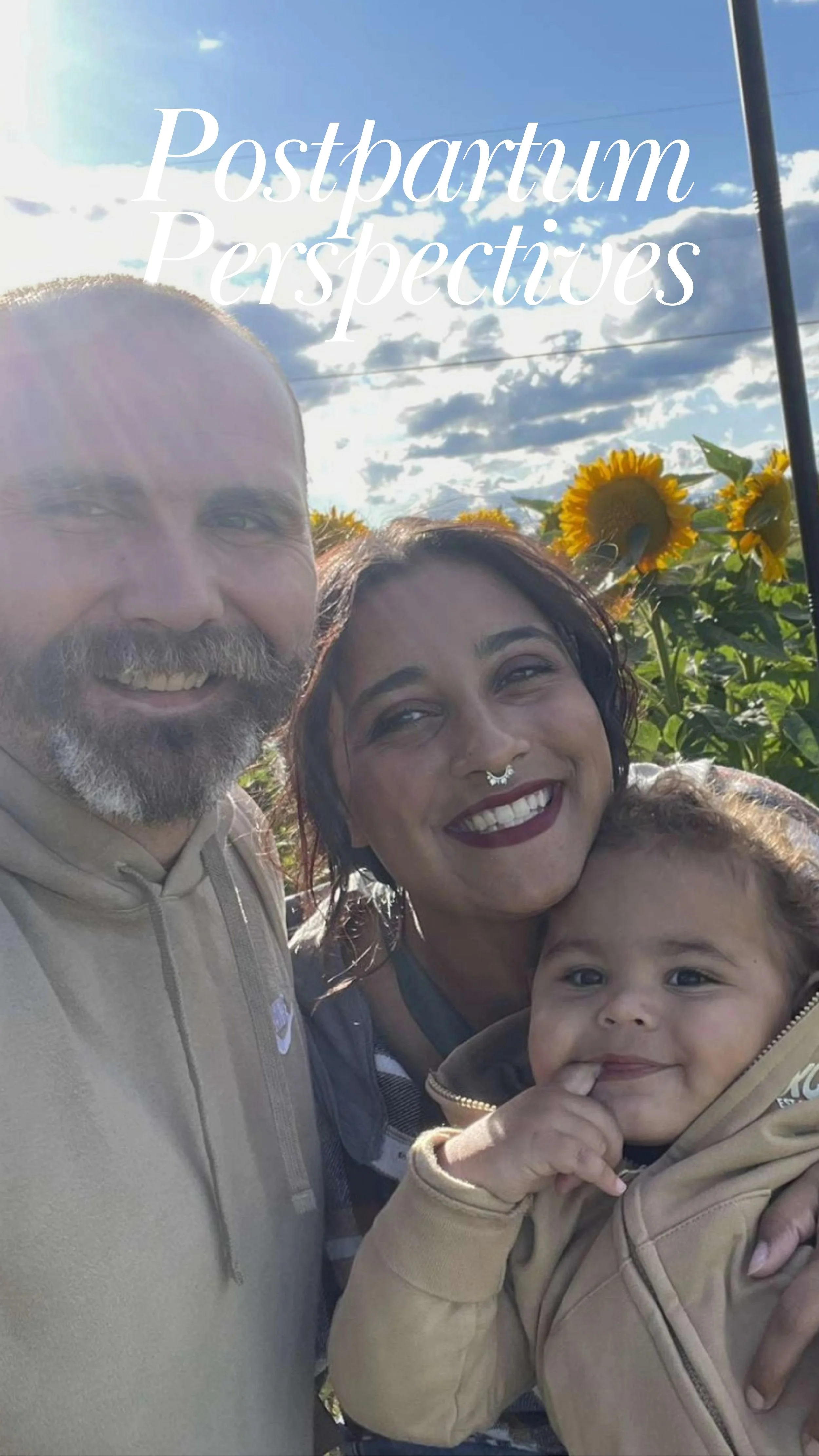 A mom and dad standing in a sunny sunflower field holding their smiling toddler